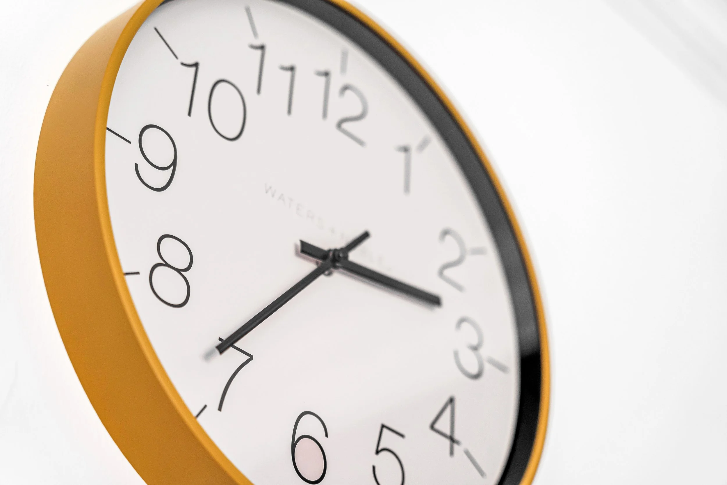 Yellow wall clock with white face showing the time as 11:11, with black hour, minute, and second hands, mounted on a white background.