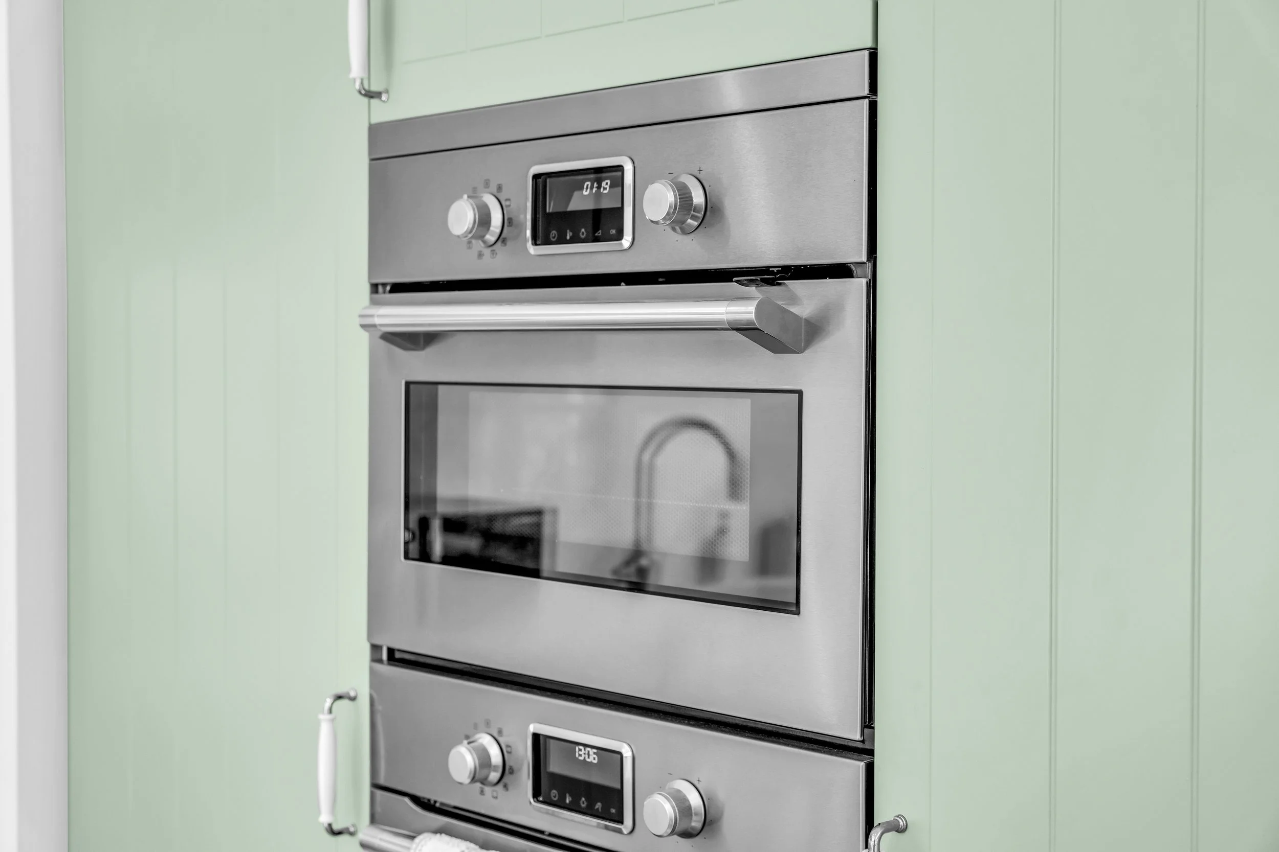 Stainless steel oven built into a light green kitchen wall with digital display and control knobs.