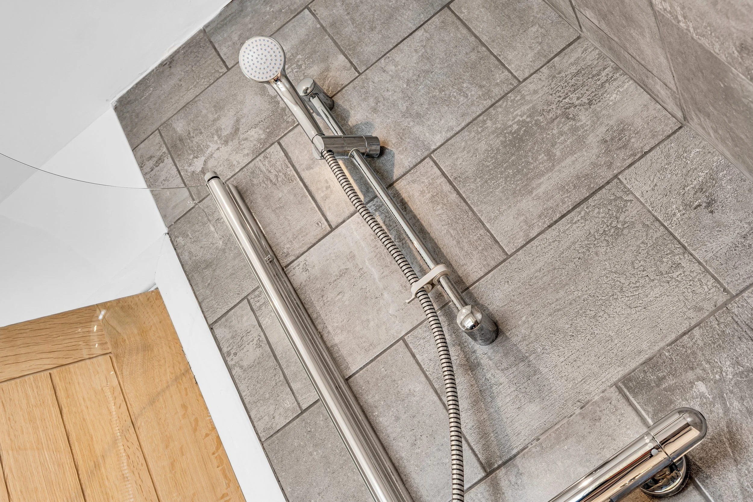 Disassembled chrome showerhead and fixtures on a tiled bathroom wall.