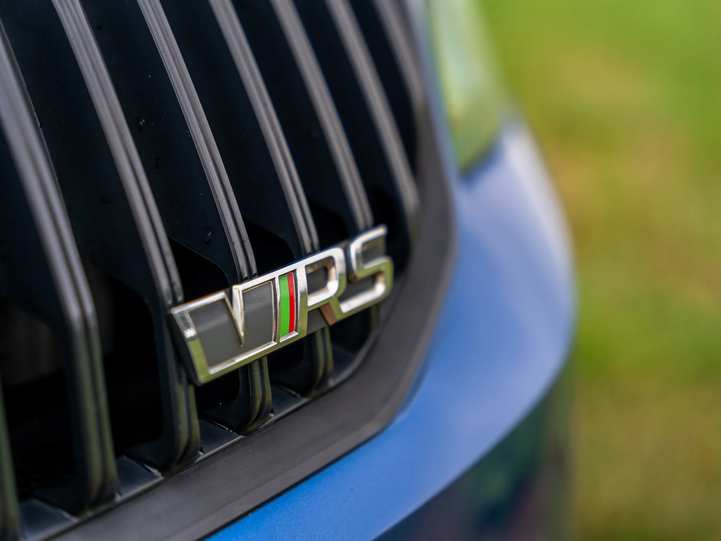 Close-up of a vehicle's grille with a VRS badge, featuring a green, white, and red stripe, on a blue car.