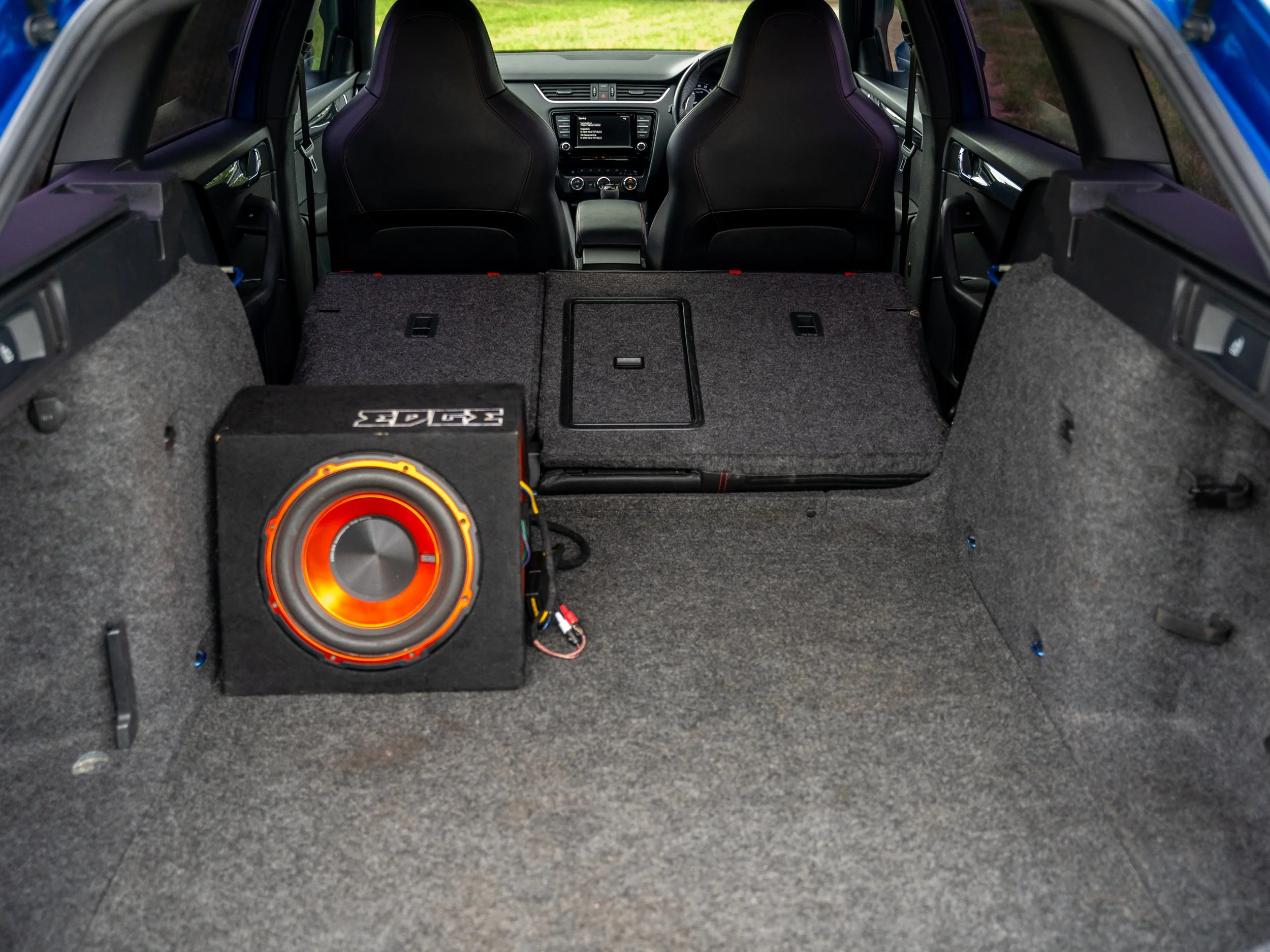 The interior of a car showing the back seats folded down with a subwoofer speaker installed in the trunk.
