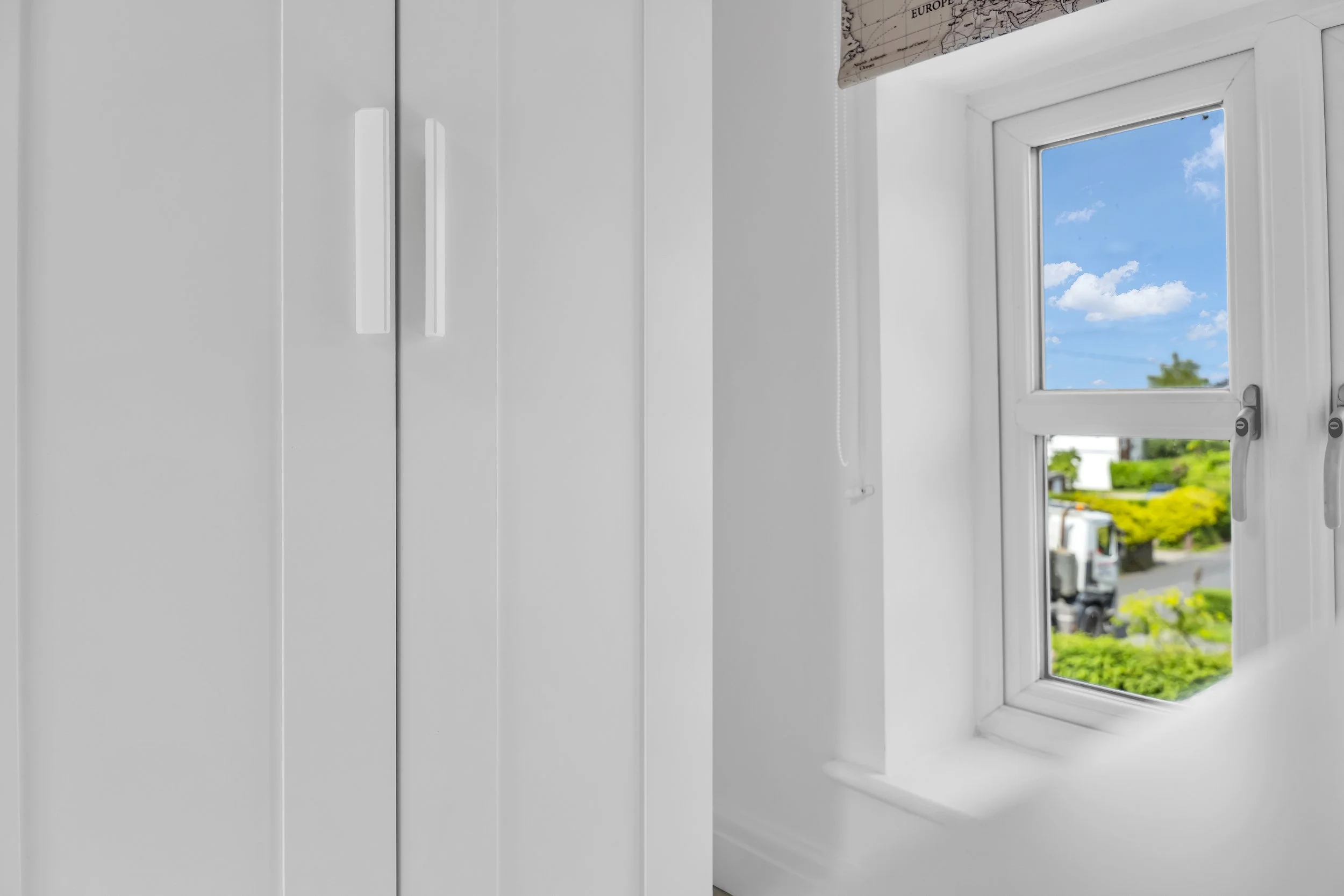 A white window with a view of a blue sky with clouds and green trees outside.