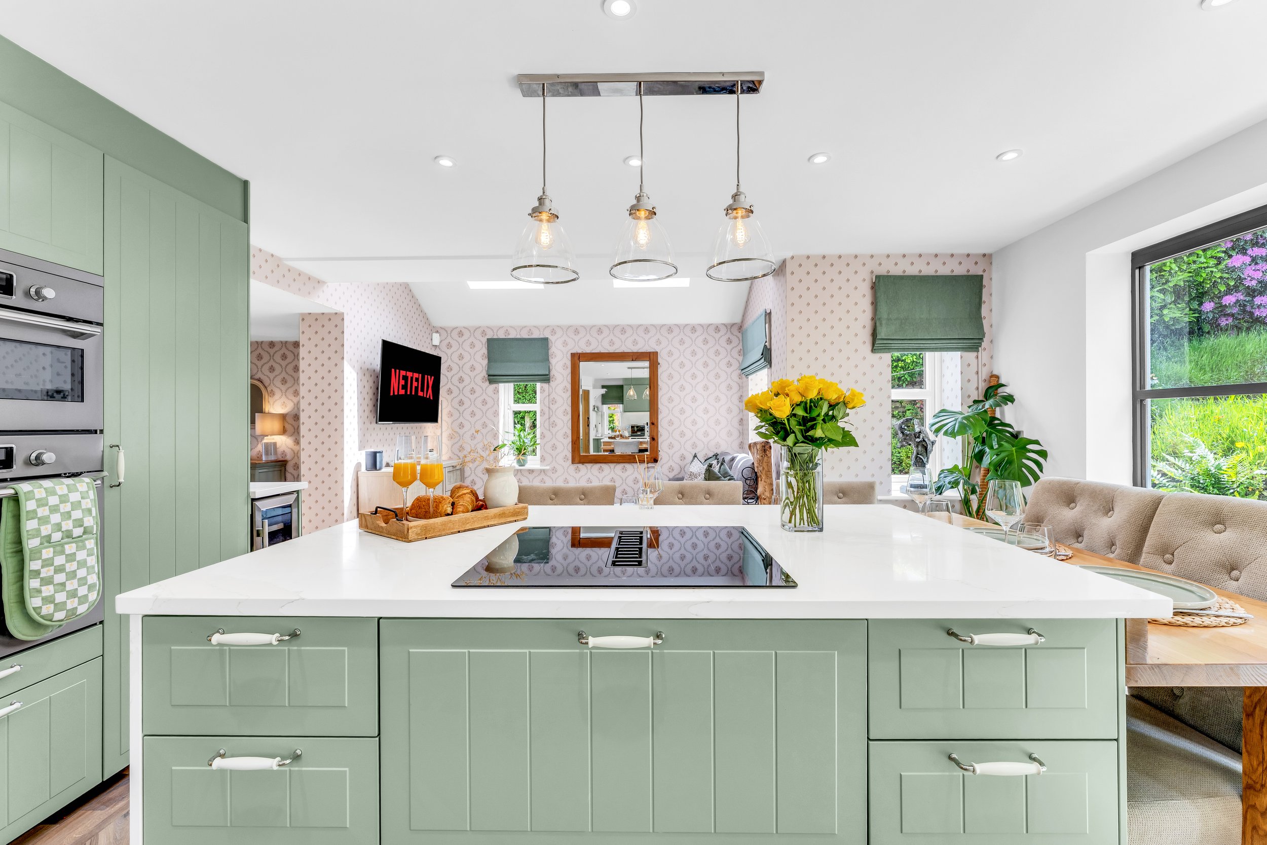 Kitchen with green cabinets and a white countertop island, decorated with a vase of yellow flowers and two glasses of orange juice.