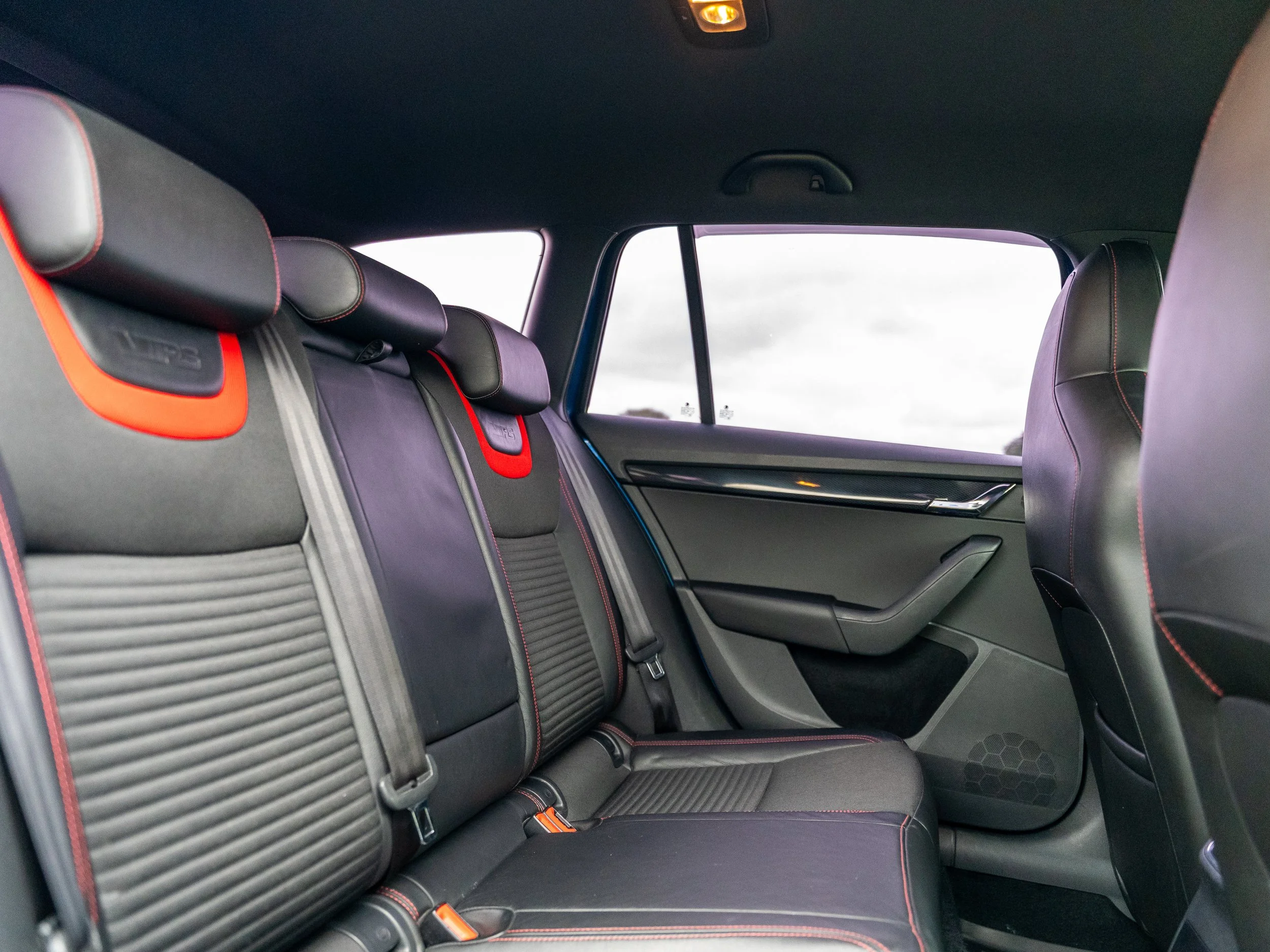 Interior of a modern car showing black leather seats with red stitching and headrest, rear side window, and door panel.