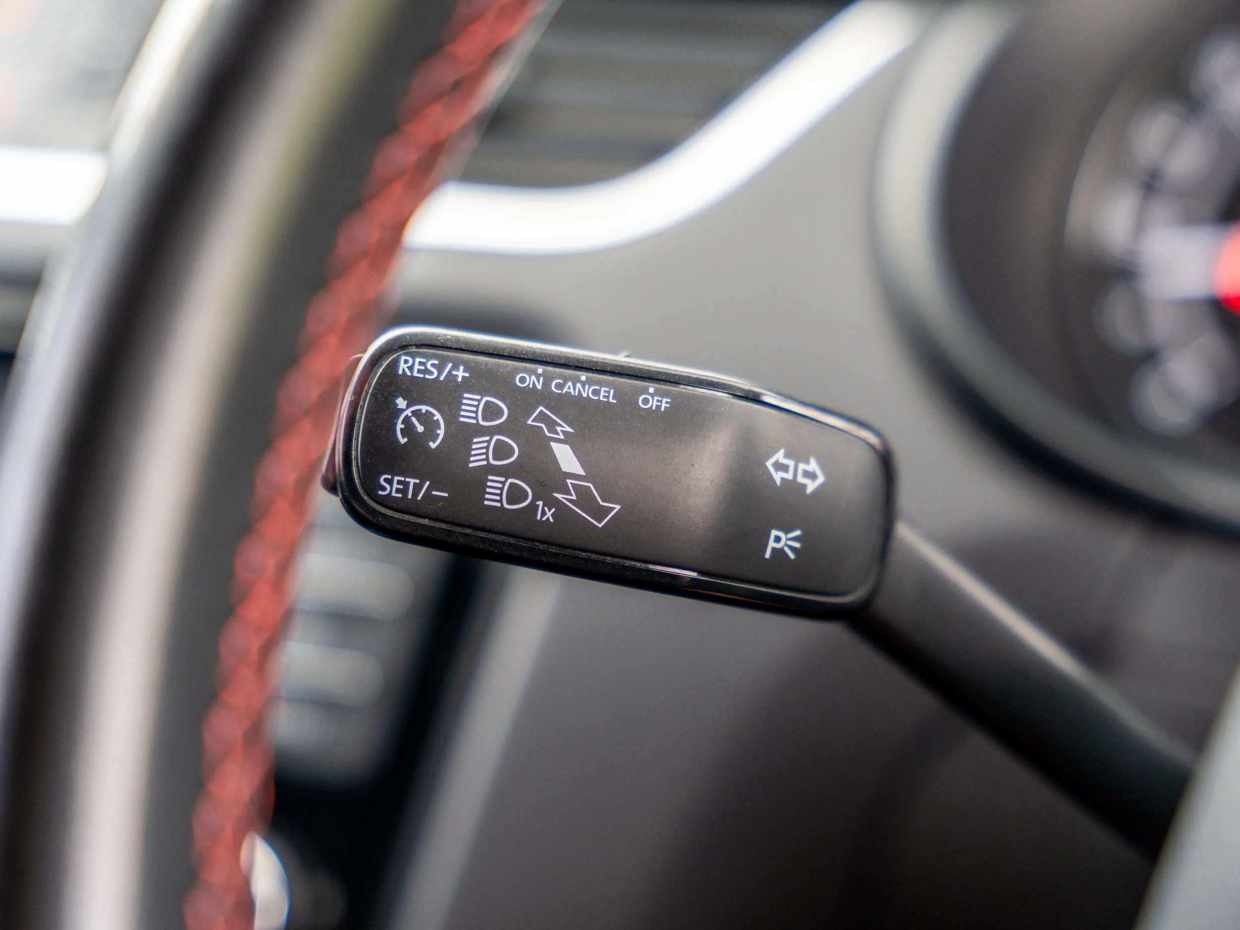 Close-up of a car's steering wheel with cruise control and turn signal control stalk, featuring icons for headlight and parking light functions.