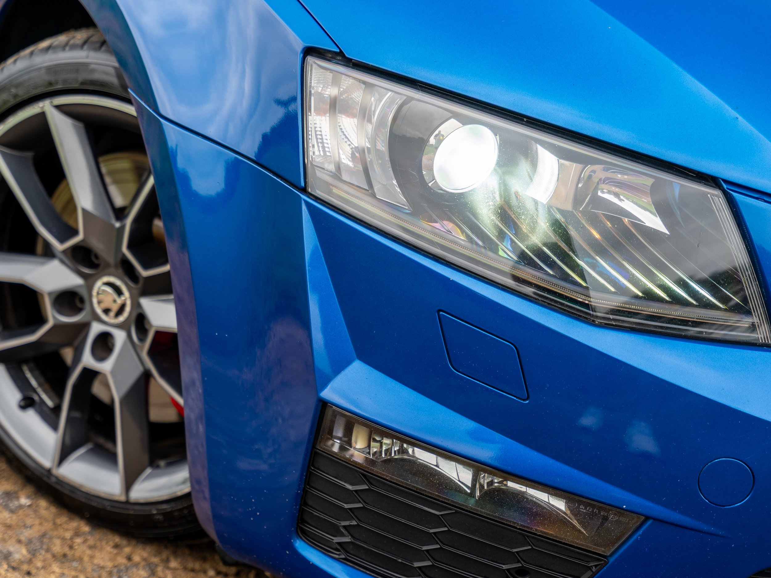 Close-up of the front right side of a blue sports car, showing the headlight, tire, and front grille.