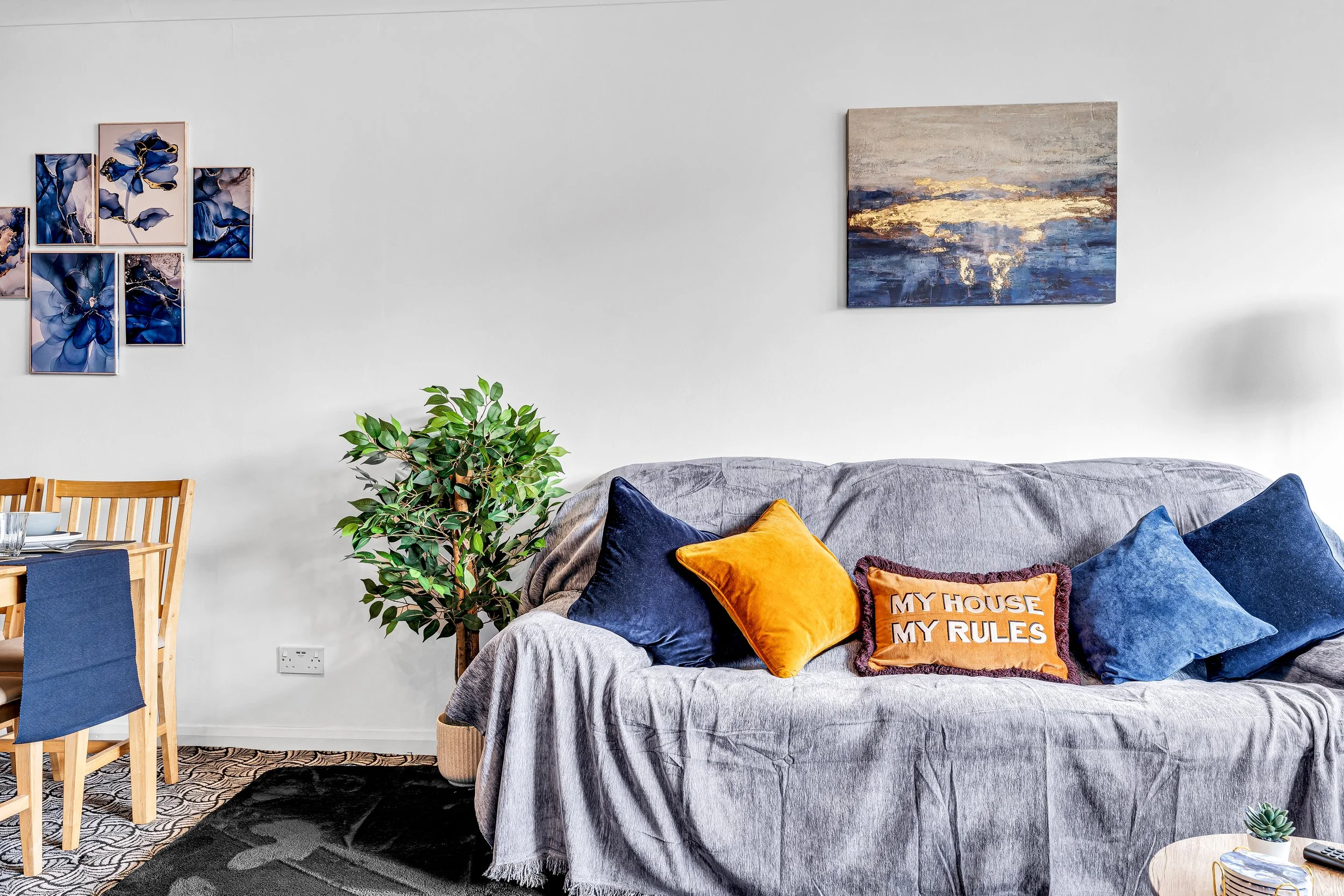 Living room with a gray sofa adorned with colorful pillows, a potted plant, and wall art.