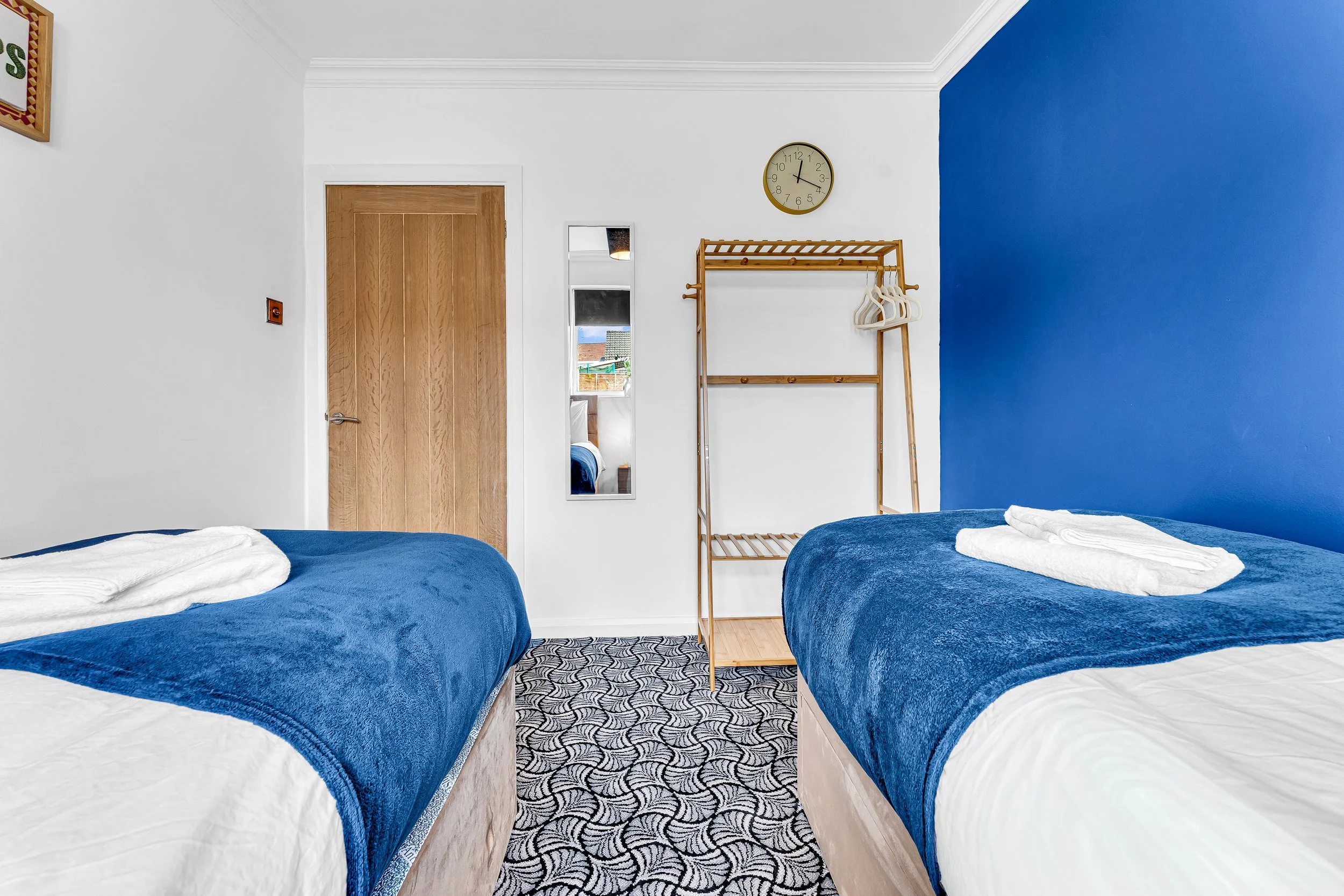 A hotel room with two beds covered in blue blankets, towels on top, a wooden door, a mirror, and a blue accent wall.