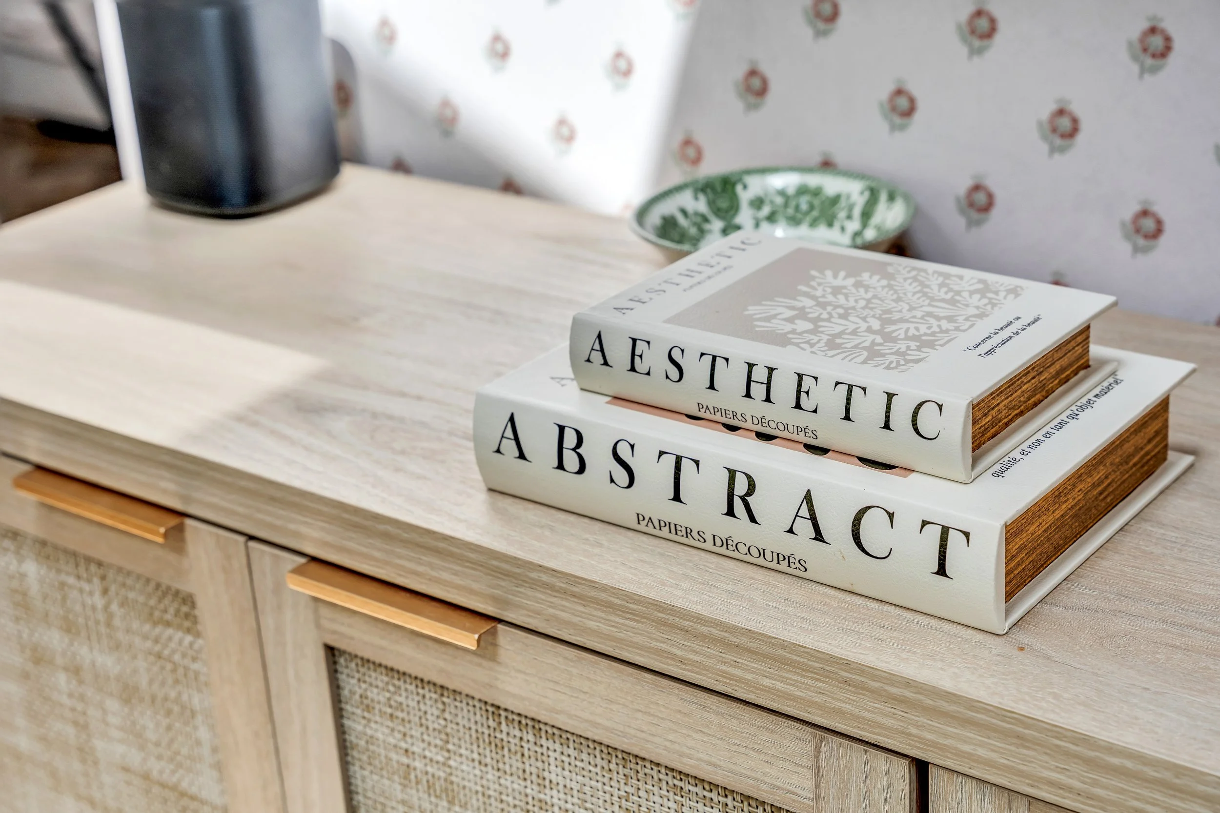 A wooden dresser with three stacked books titled "Aesthetic," "Abstract," and "Papiers Découpés" on top of it, with a green decorative plate and an air fryer in the background.