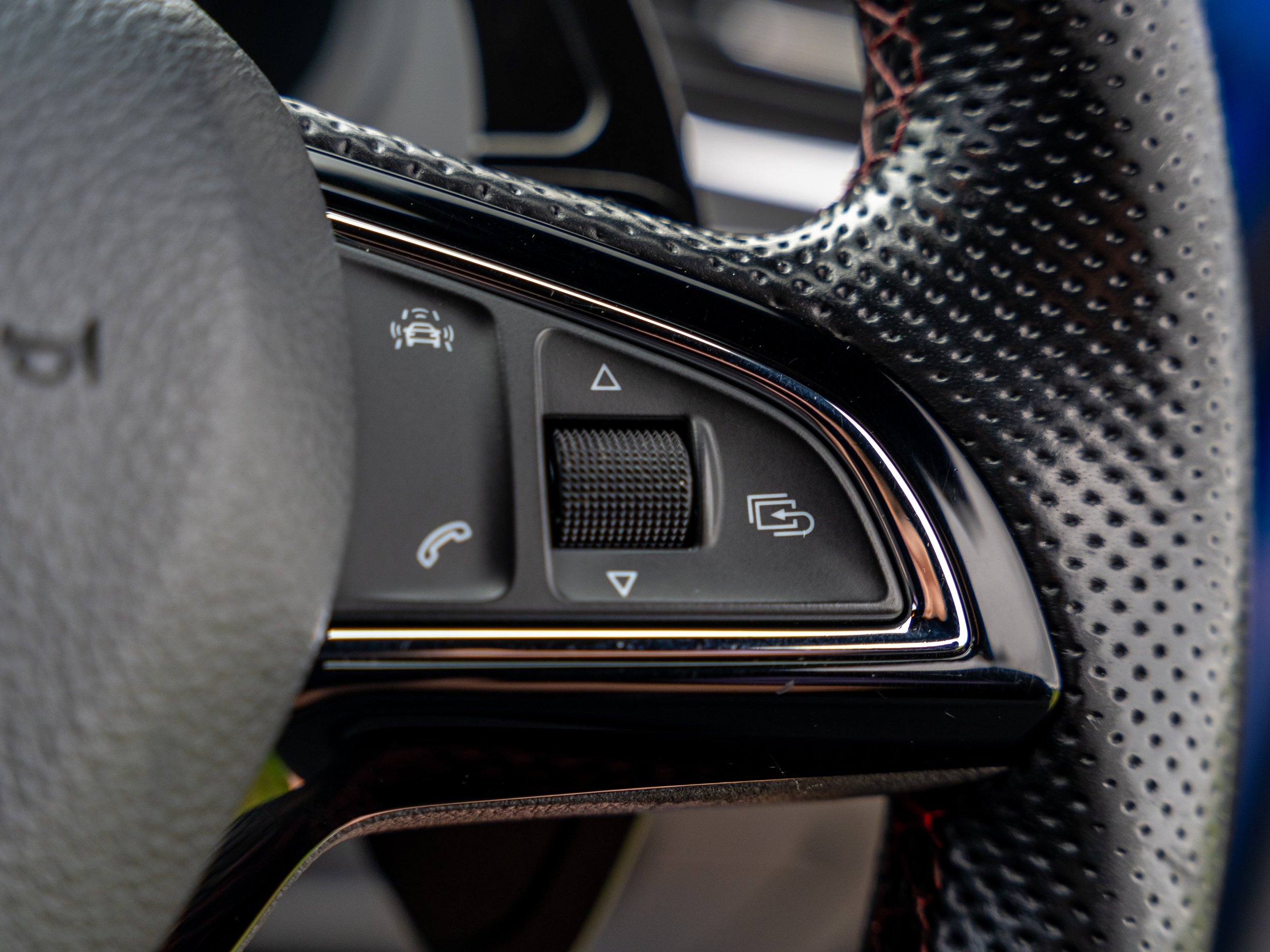 Close-up of a car steering wheel with control buttons, including phone and voice command icons, and textured grip material.