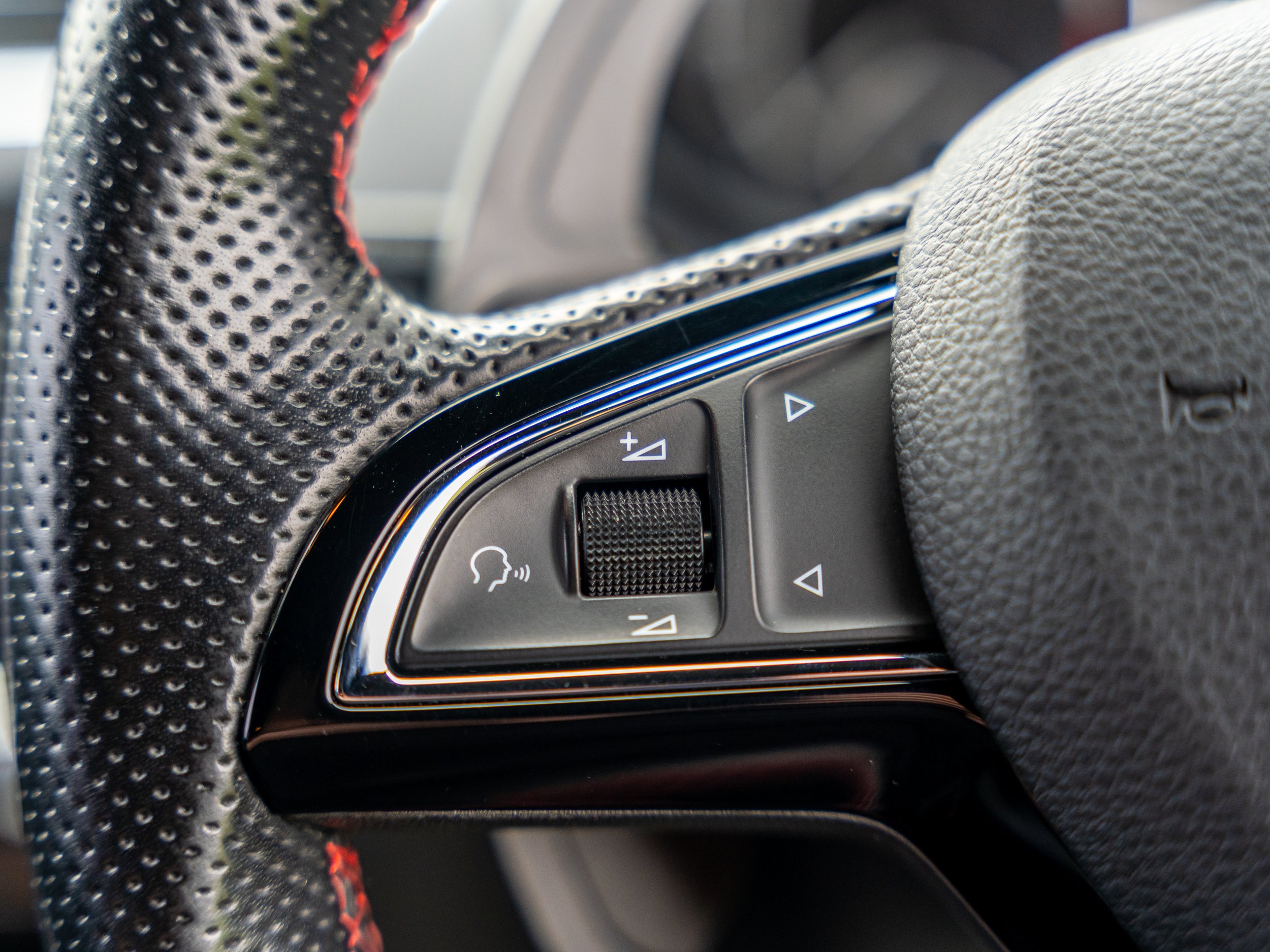 Close-up of a car steering wheel with control buttons and textured grip with red stitching.