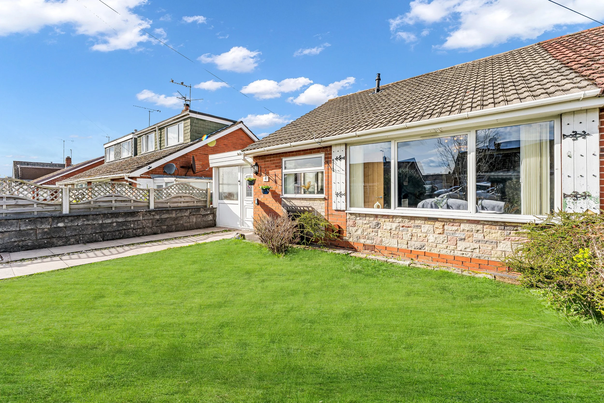 Front view of a brick house with a large window and a small garden, under a blue sky with clouds.