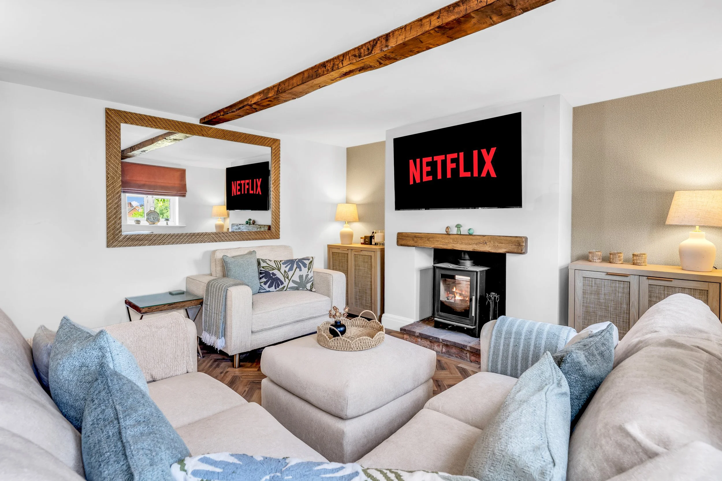 Living room with beige sofas, pillows, a mirror, a TV showing Netflix, a fireplace, lamps, and decorative items.