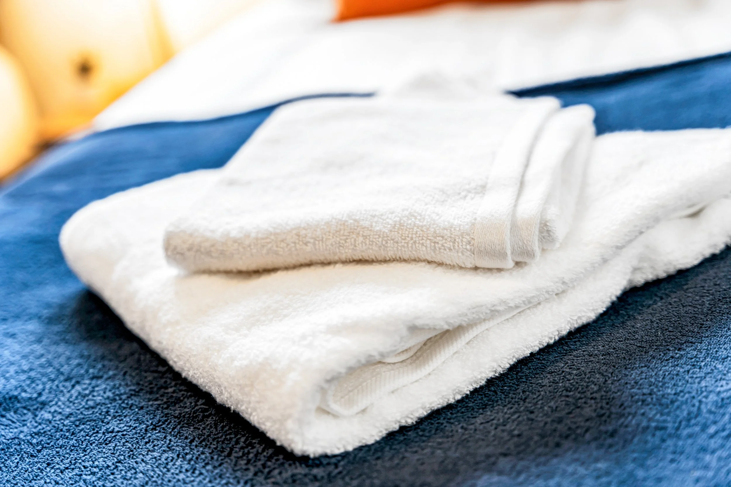 Folded white towel and a pair of white underwear placed on a dark blue fabric surface.