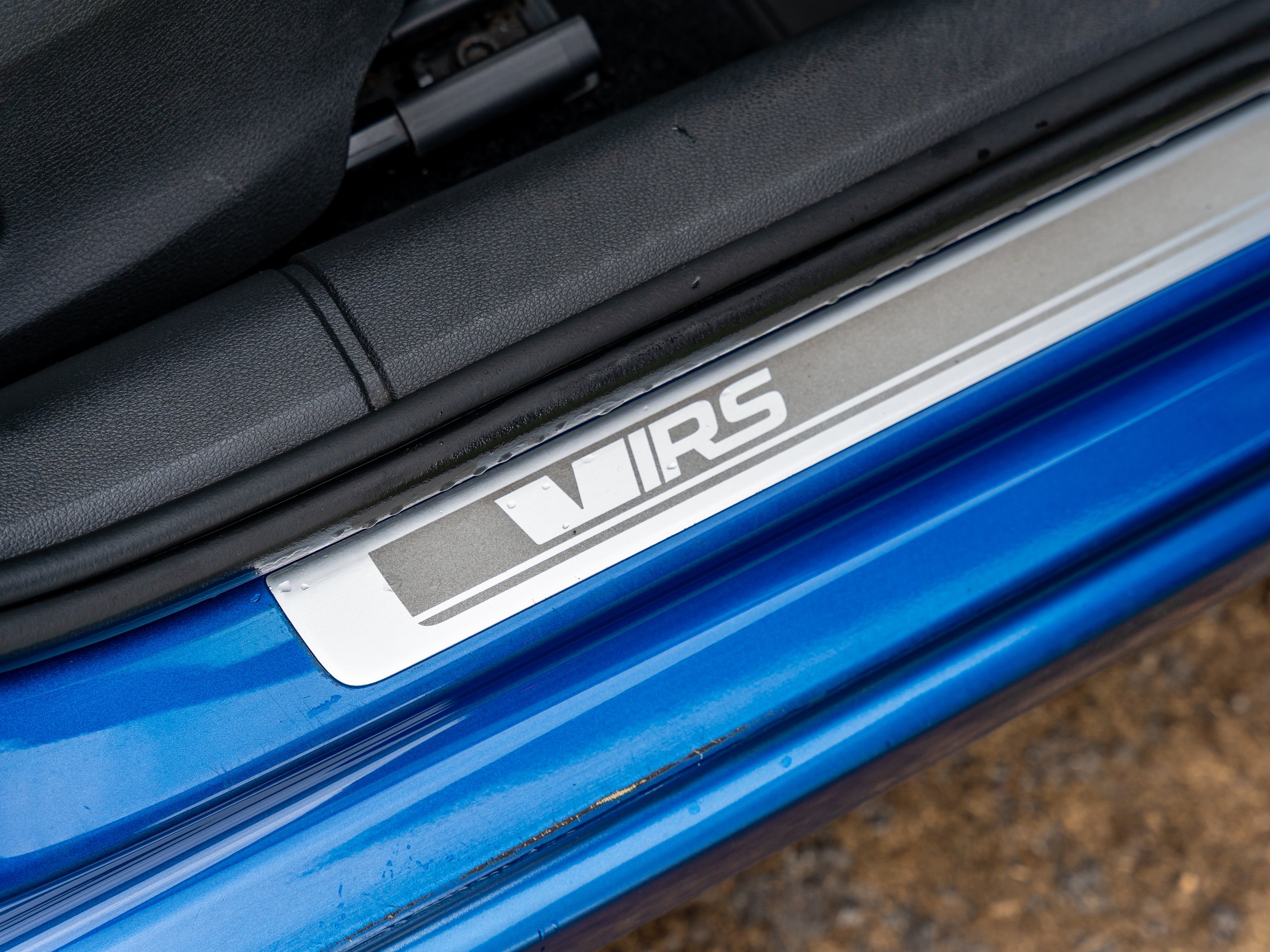 Close-up of a car door sill with a white decal that says VIRS against a blue car body.