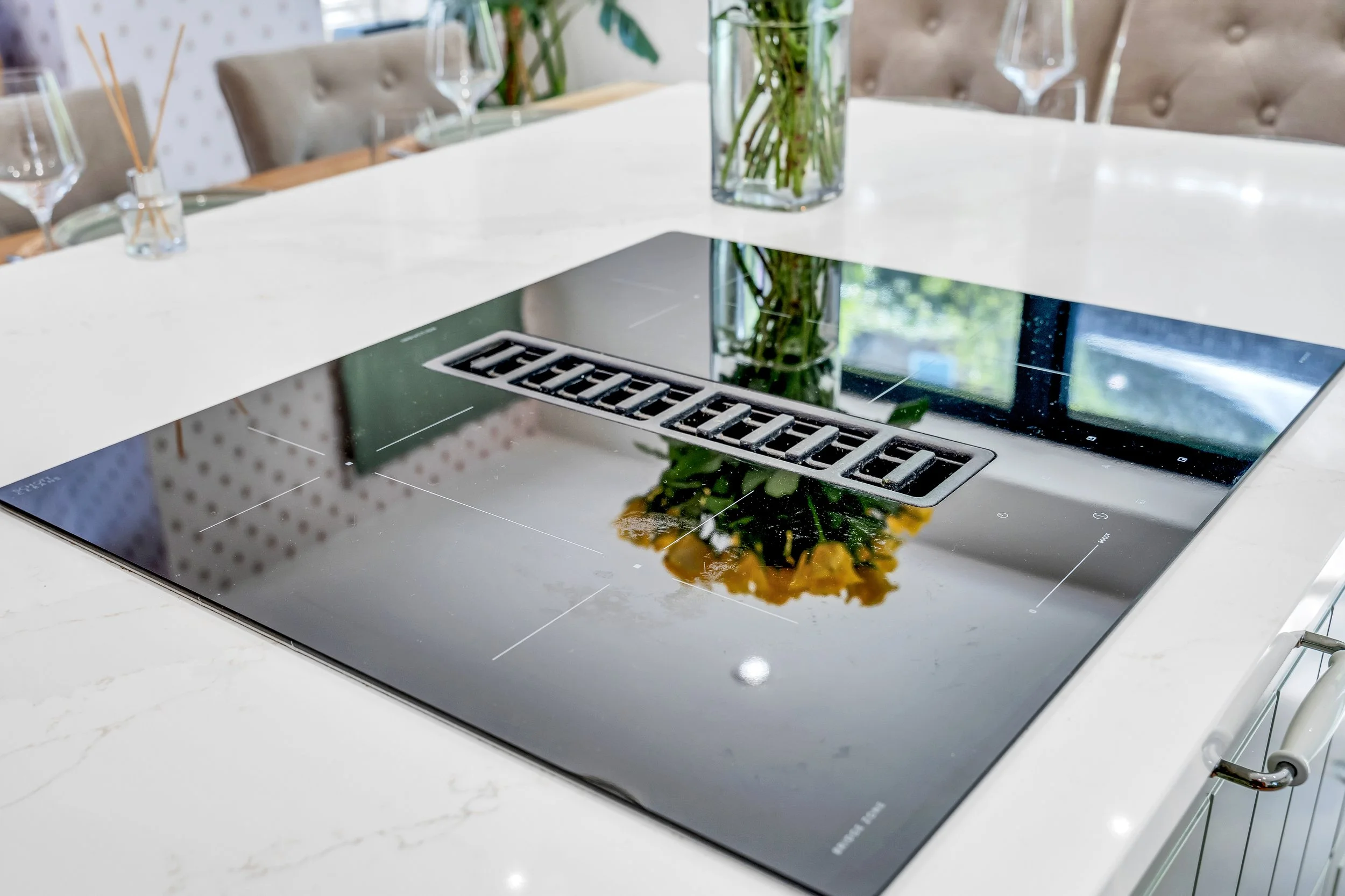 Modern black induction cooktop with a reflective surface, built into a white kitchen countertop, with a decorative vase containing green plants in the background.