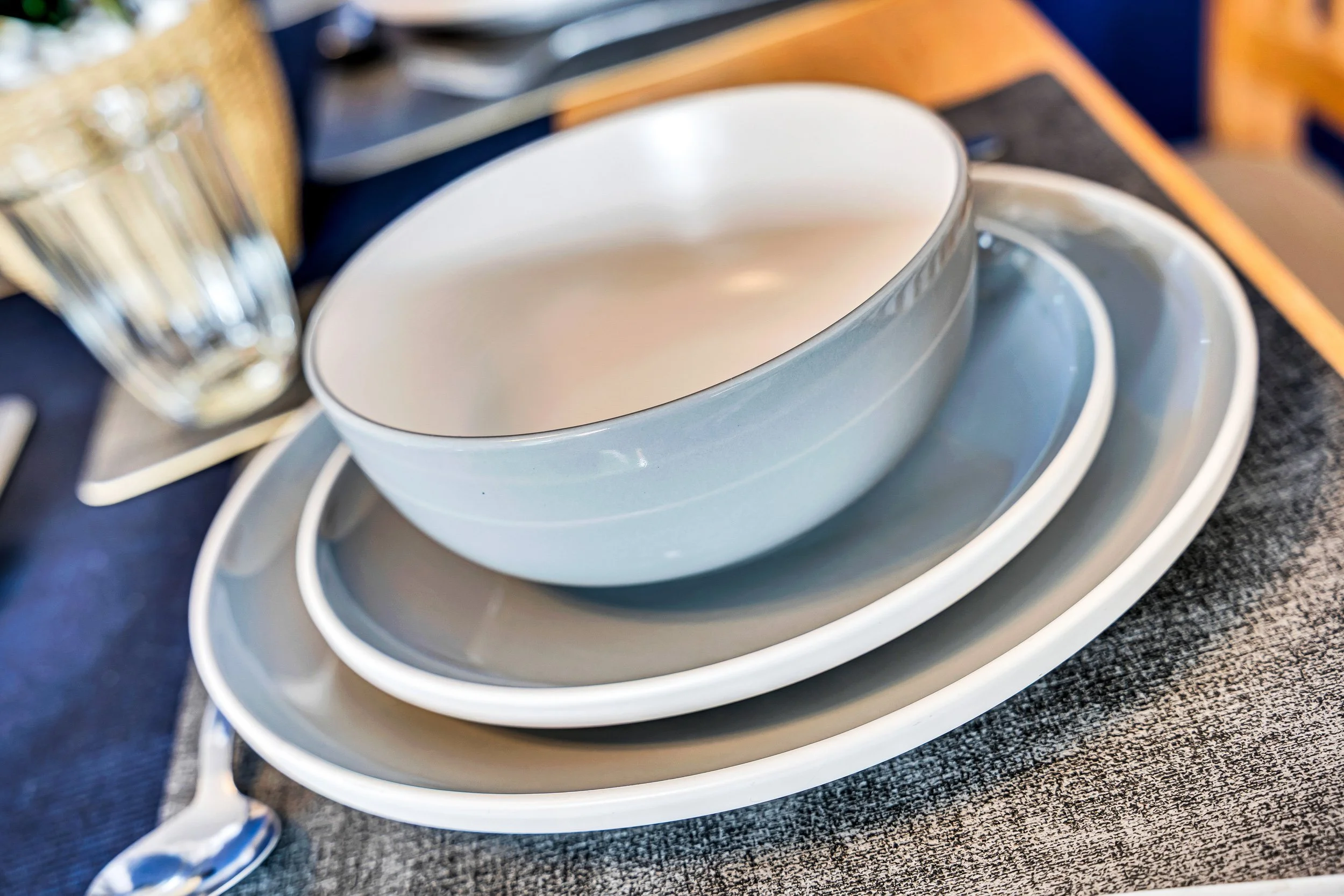 Stacked white and gray dishes and bowls on a table setting.