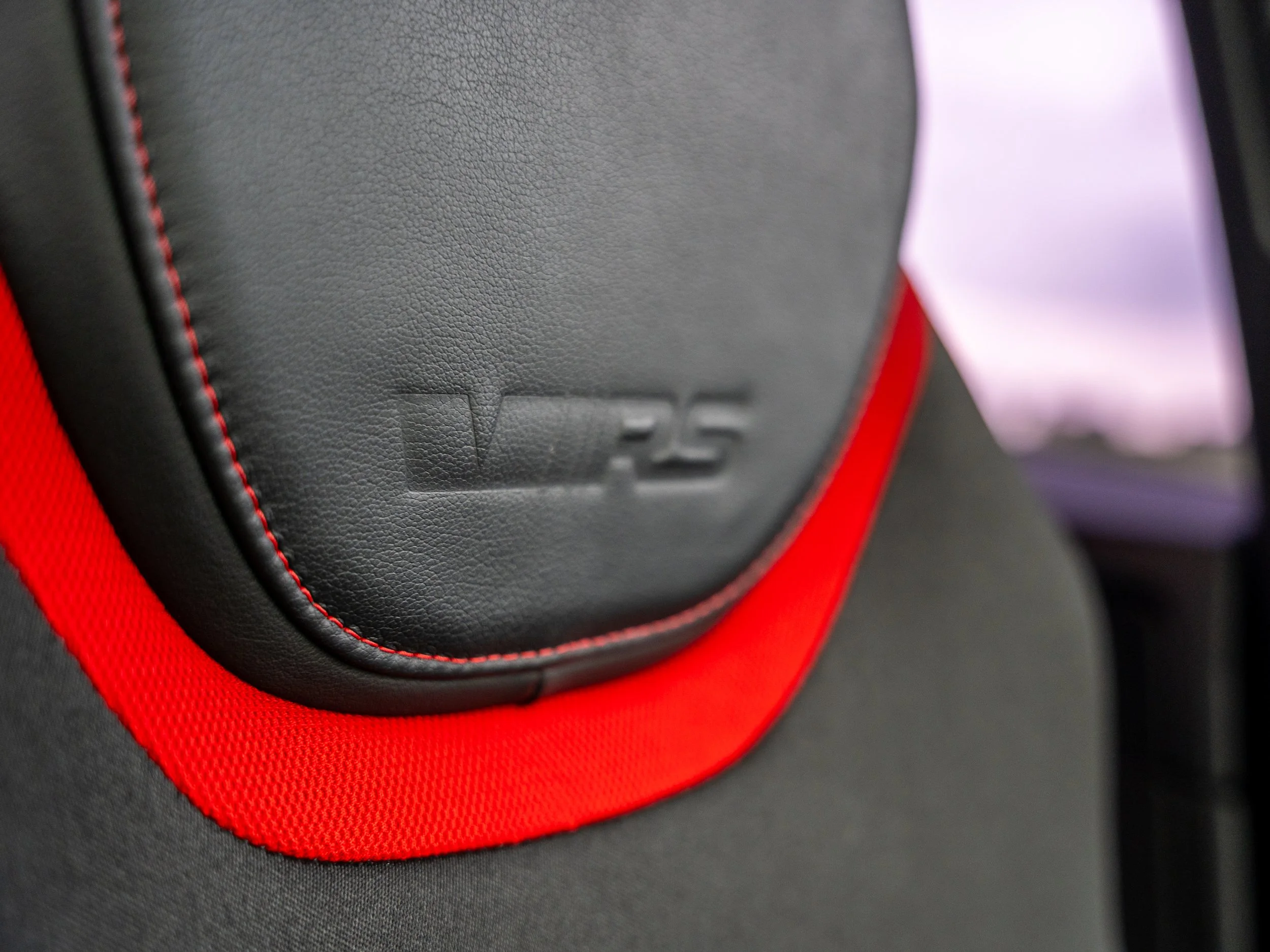 Close-up of a car seat with a black leather headrest featuring the embossed JBL and 25 logos, surrounded by red fabric.