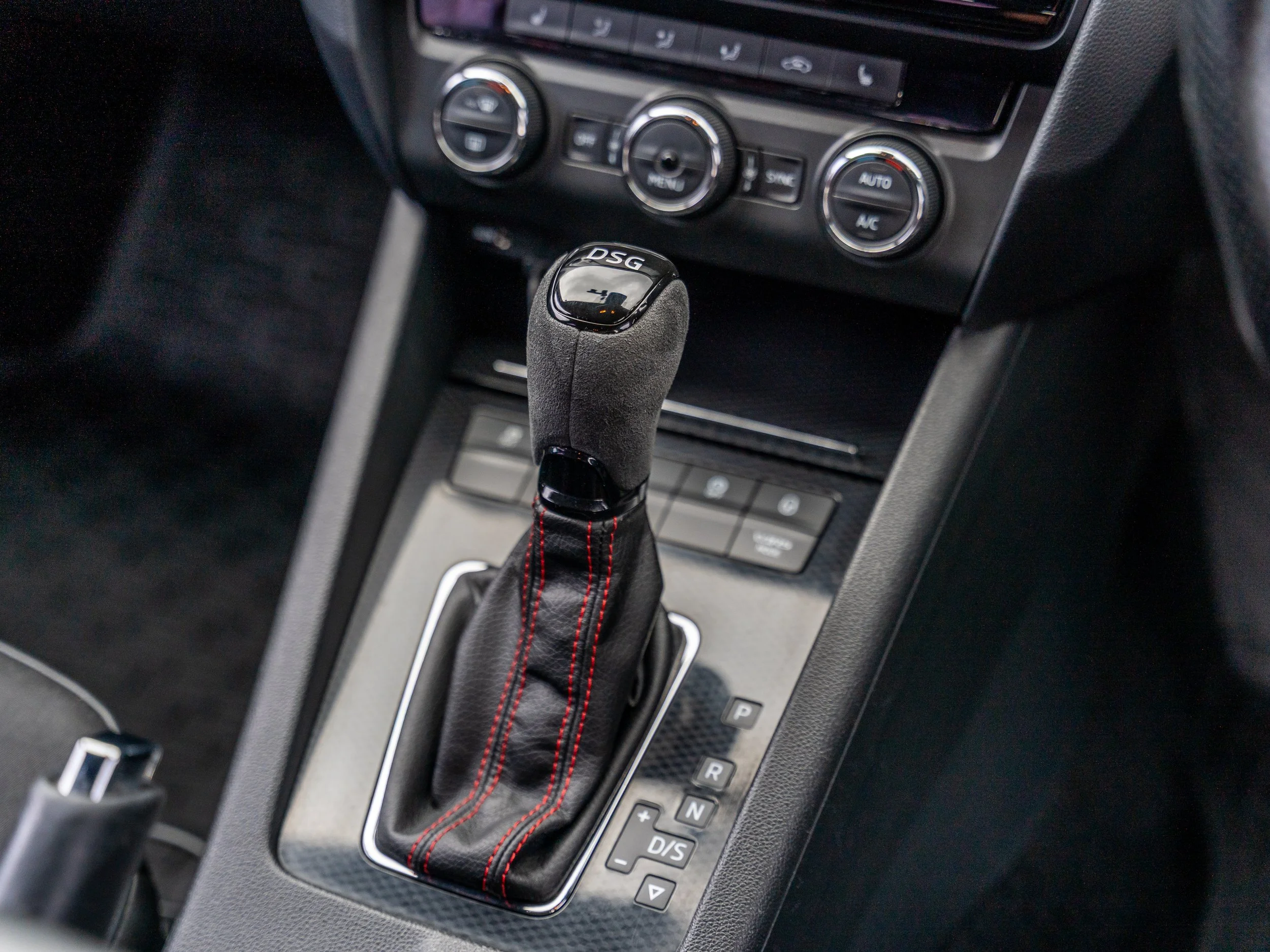 Close-up of car gear shift lever in an interior vehicle, with climate control dials and dashboard controls visible in the background.