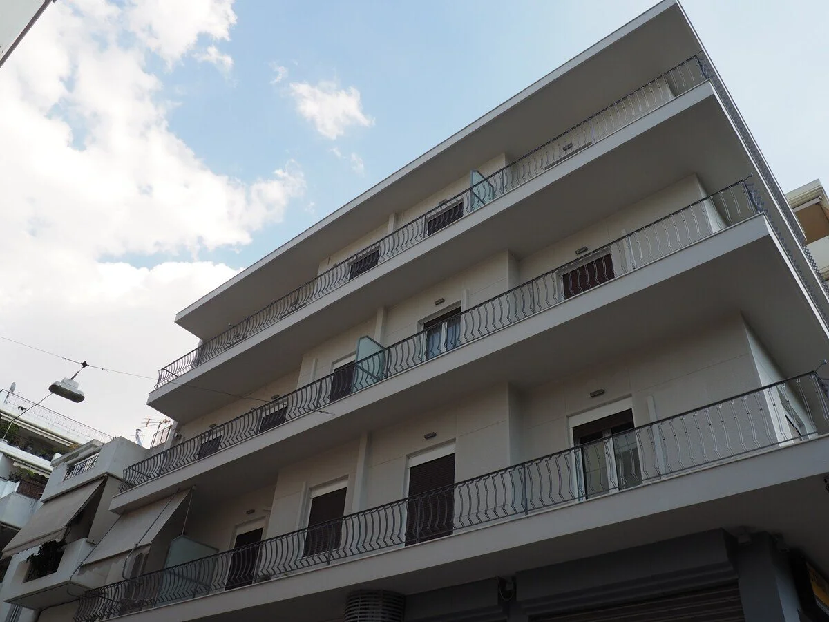 A white multi-story apartment building with balconies and black railings, under a partly cloudy sky.