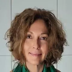 A woman with curly, shoulder-length hair, smiling softly, wearing a green top.