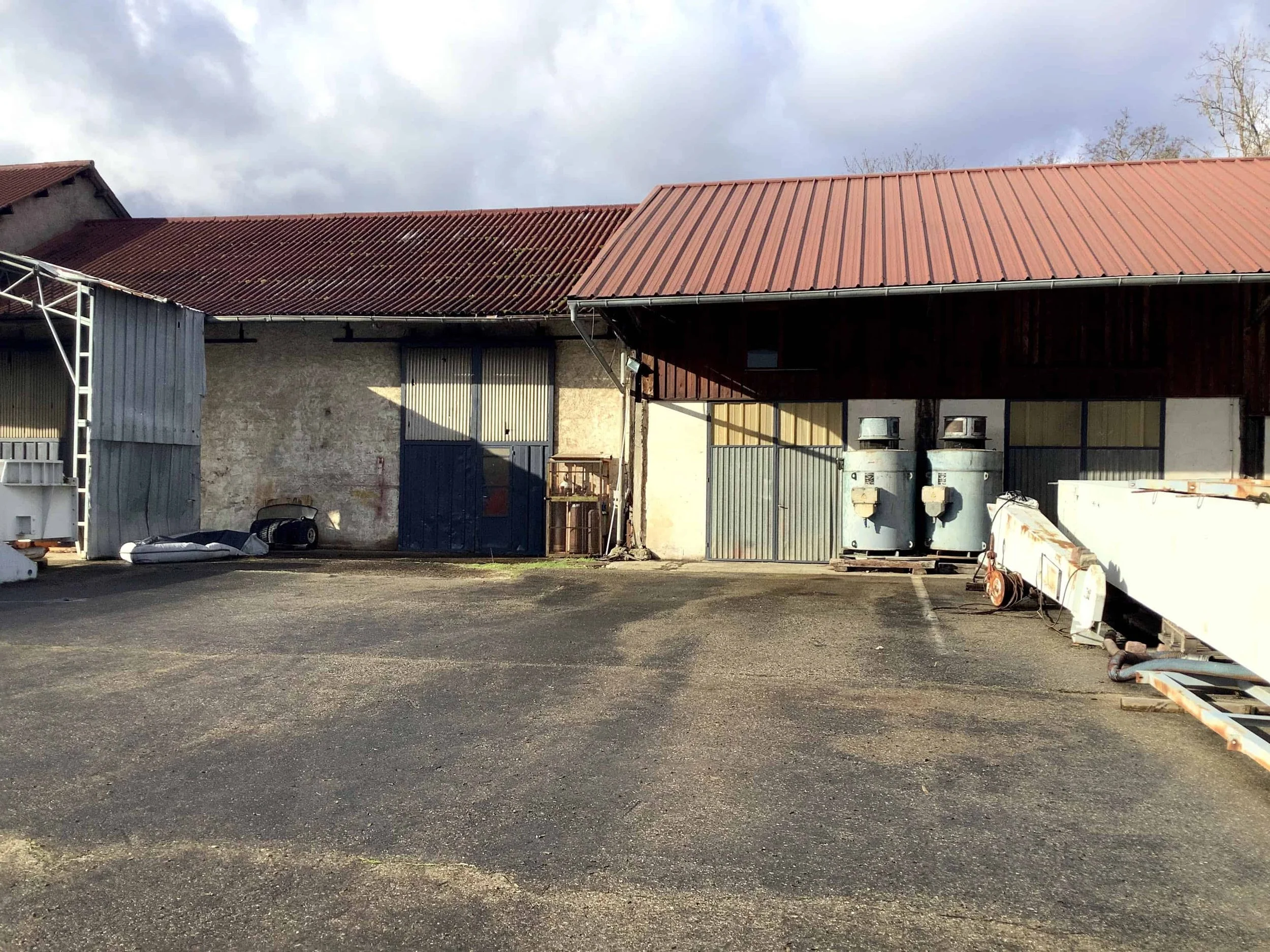 Vue extérieure de bâtiments industriels accolés avec toitures en tôle et grandes portes de garage, destinés à devenir une élégante salle de fête. L'architecture utilitaire avant sa métamorphose. Aimeriez-vous conserver cet esprit industriel sur la fa