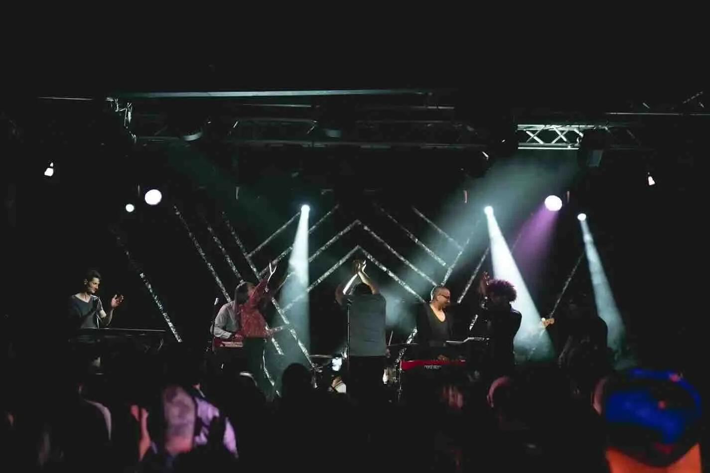 Une installation scénographique artistique pour un concert avec une structure lumineuse circulaire LED éclairant des musiciens sur une scène sombre. Design d'espace scénographique à Genève.