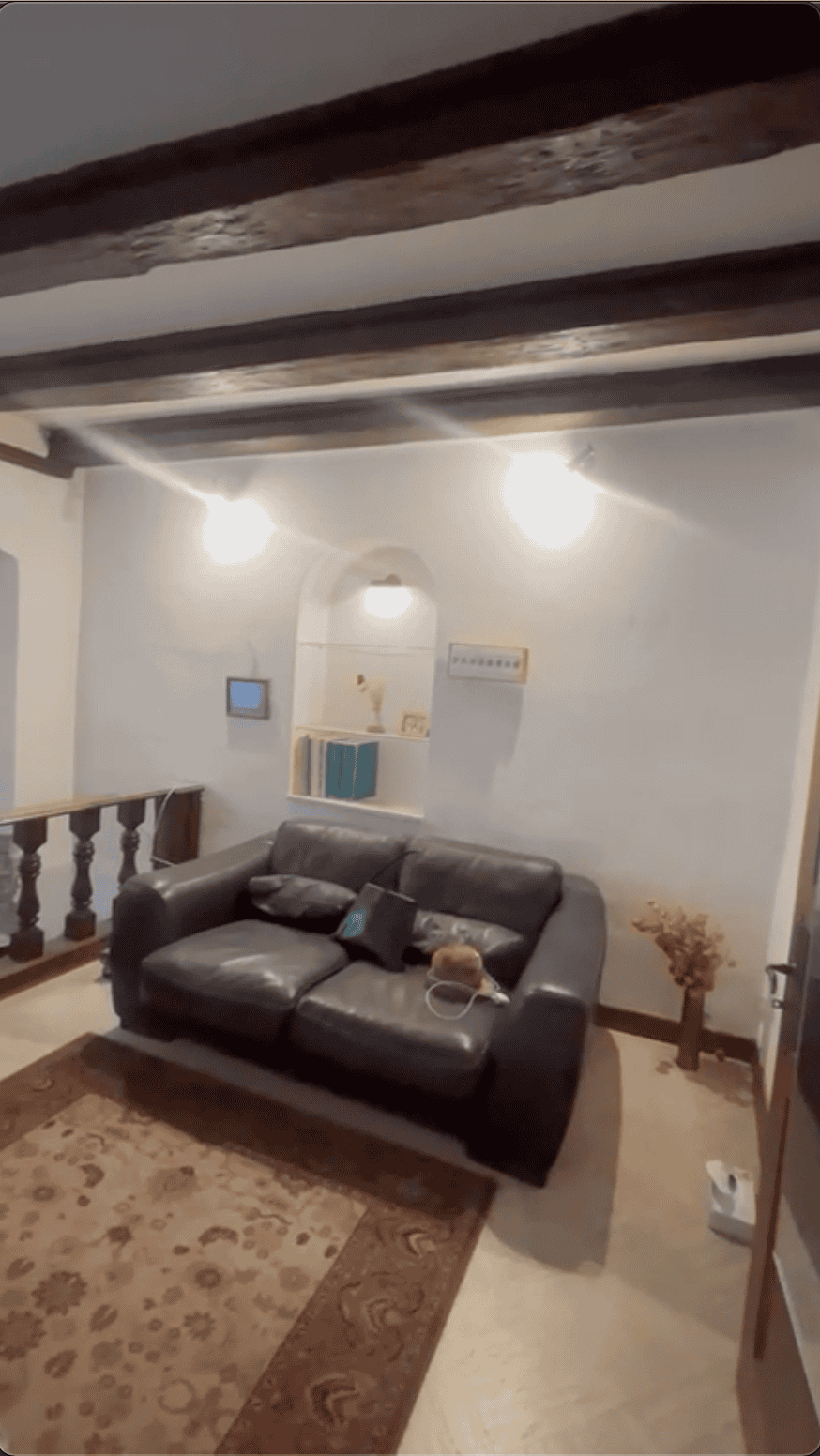 Espace de vie sous charpente avec garde-corps en bois tourné et canapé, montrant l'agencement et les volumes avant la transformation.