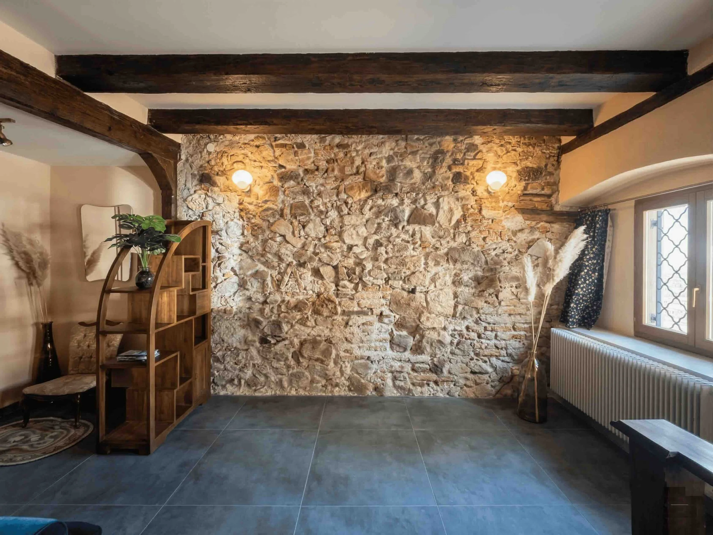 Rénovation intérieure par un architecte à Genève : salon avec mur porteur en pierre naturelle et briques apparentes, poutres en bois d'origine et design contemporain.