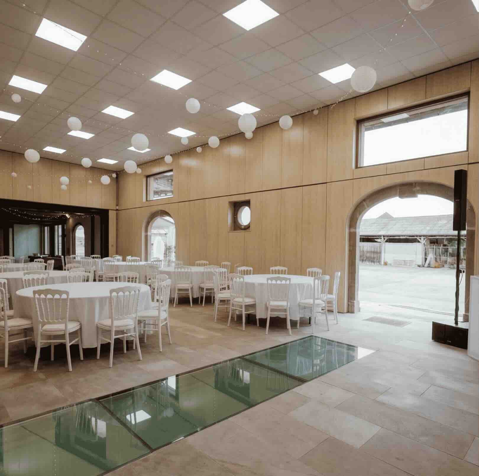 Détail du sol d'une salle de réception à Genève : une impressionnante plaque de verre praticable recouvre l'ancienne fosse mécanique du garage, préservant la mémoire ouvrière du lieu au cœur du nouvel aménagement festif.