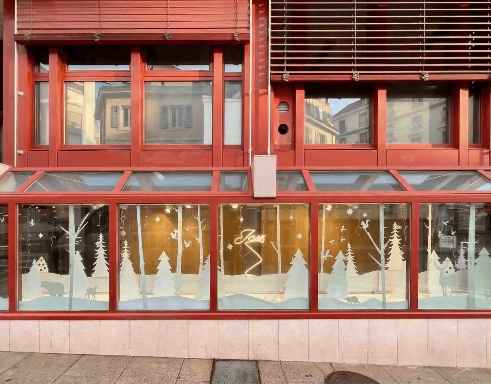 Vue de jour d'une vitrine aménagée à Genève. Ce visual merchandising en diorama de papier et bois aux lignes épurées capte la lumière.