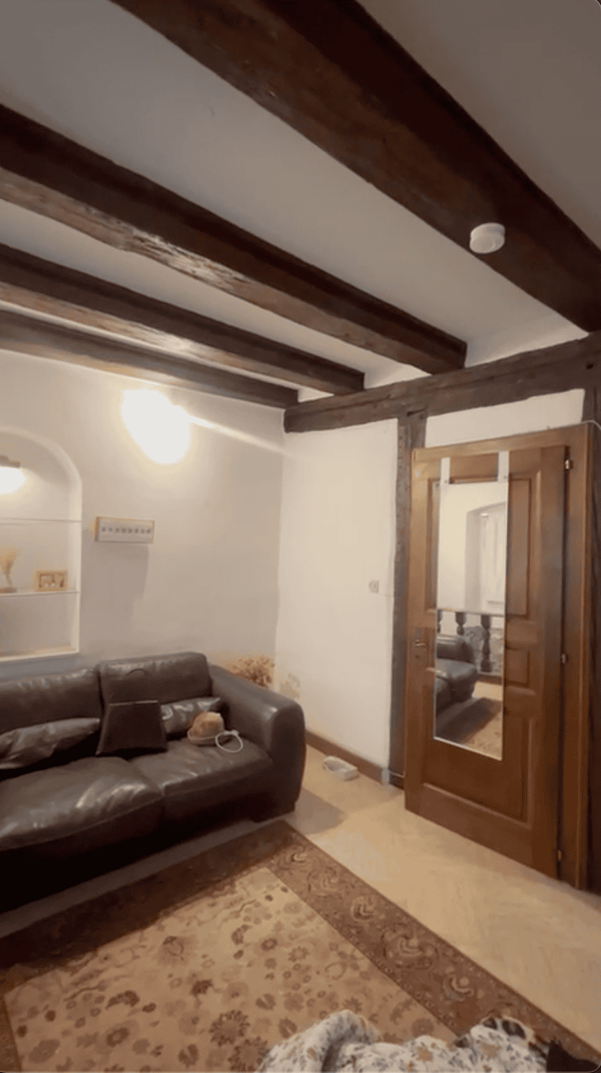 Salon existant avec poutres maîtresses sombres, boiseries et grands volumes, illustrant l'état initial avant notre projet de réaménagement.