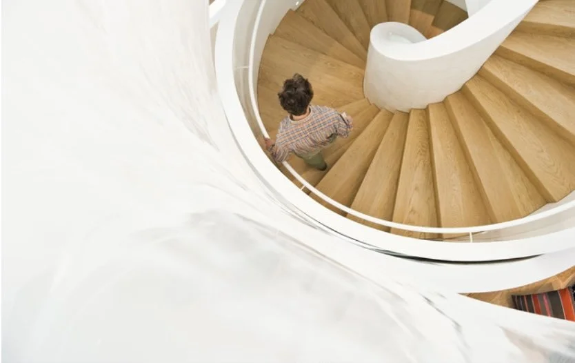 Vue plongeante sur un escalier du VitraHaus en colimaçon en bois aux courbes épurées. Un véritable élément architectural et sculptural mis en valeur. Un colimaçon pour votre rénovation à Genève.