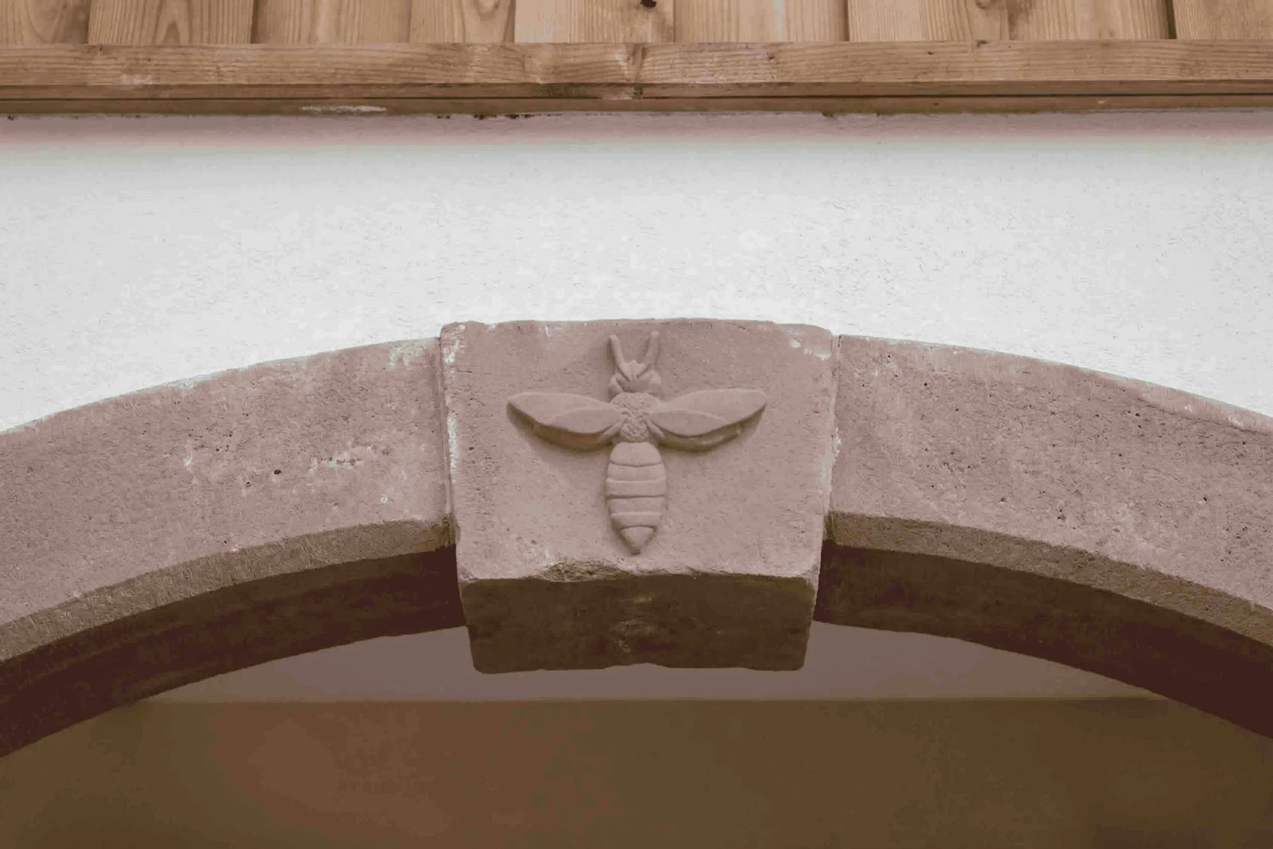 Gros plan sur une clé de voûte en pierre de taille ornée d'une abeille sculptée sur mesure. Ce blason familial, dessiné par notre bureau d'architecte, personnalise la structure de la salle de réception en l'honneur des propriétaires apiculteurs Genèv