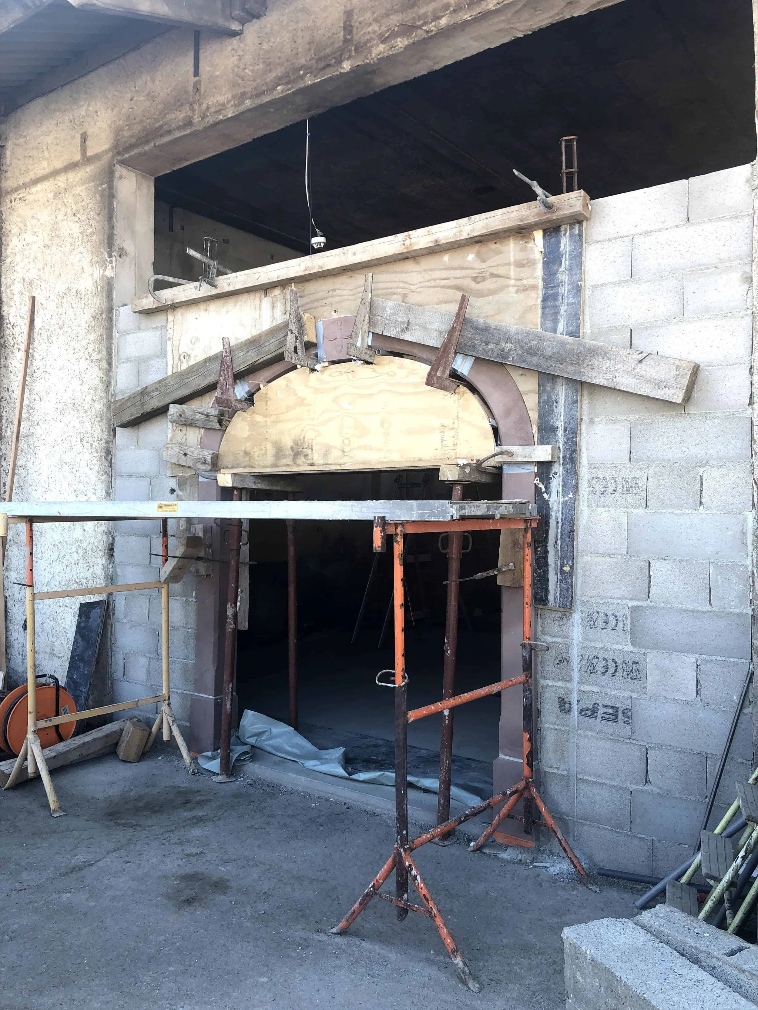 Chantier de transformation intérieure montrant la maçonnerie et la création d'une imposante arche en pierre soutenue par des étais et des échafaudages. Un travail de structure complexe pour ouvrir l'espace. Le travail de la pierre brute vous inspire-