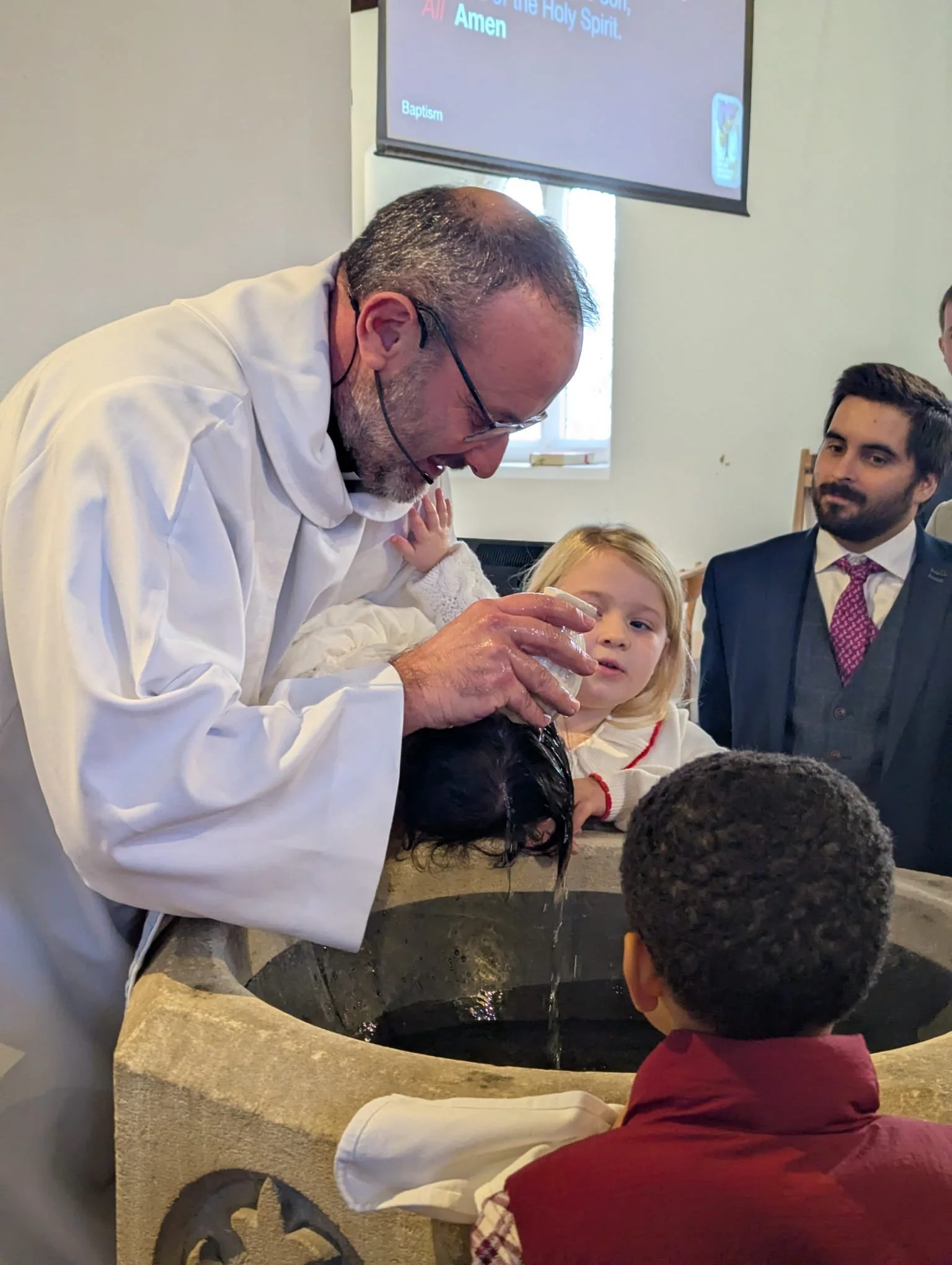 A priest baptizing a child in a church with family and friends watching.