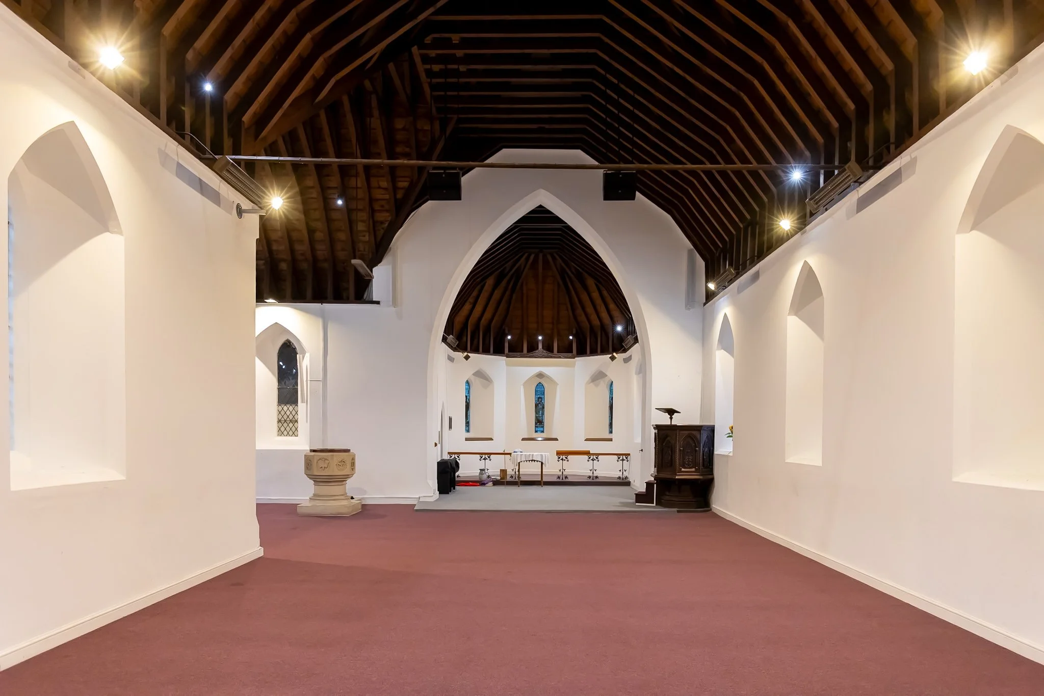 Interior of St Mary's church Sholing with white walls, wooden ceiling beams, stained glass windows, and a small altar at the front.