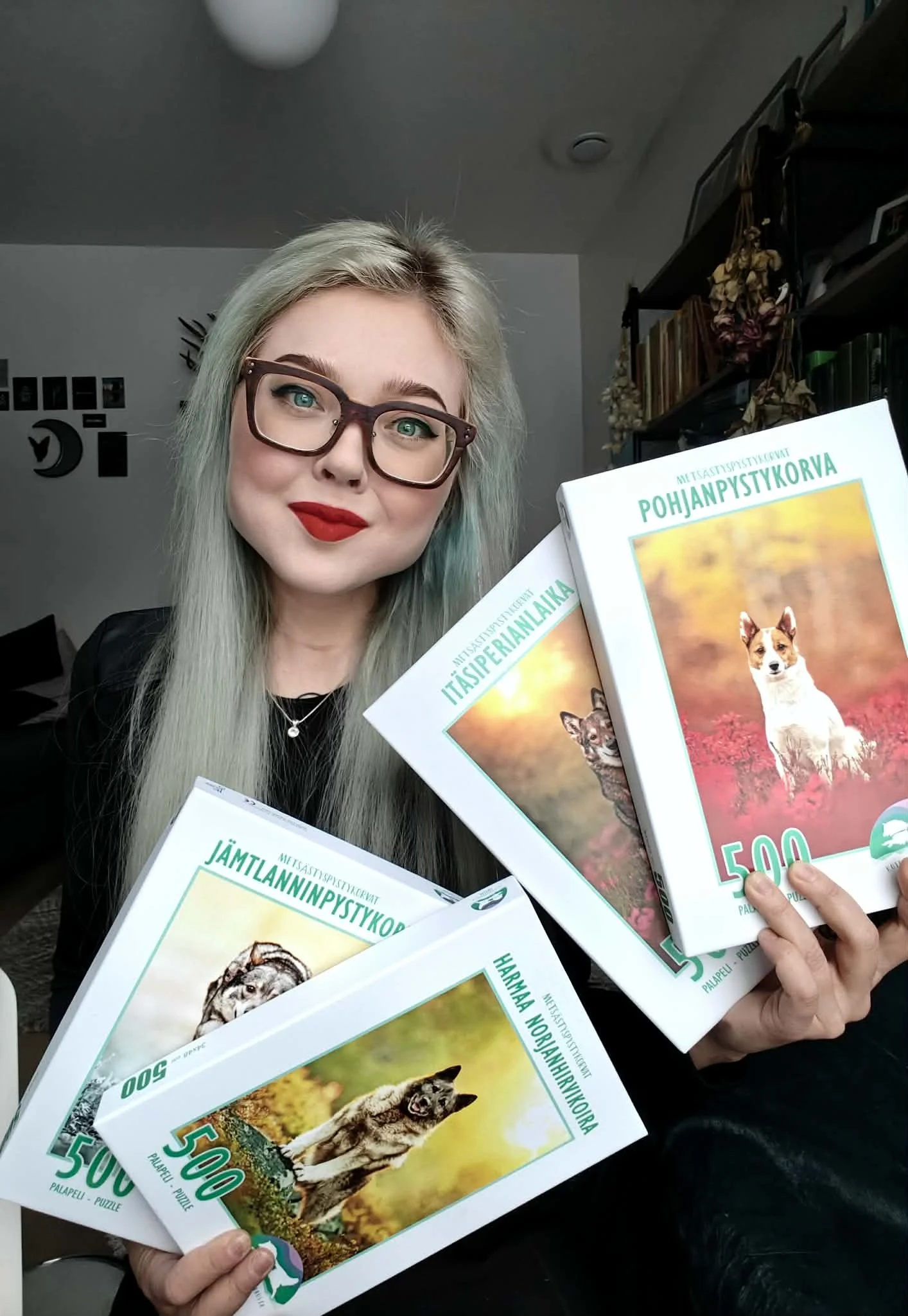 Nuori nainen, jolla on pitkät vaaleat hiukset ja punaiset huulet, pitää kolme puzzle-pakkausta, joissa on kuvia metsän ja eläinten alueista.