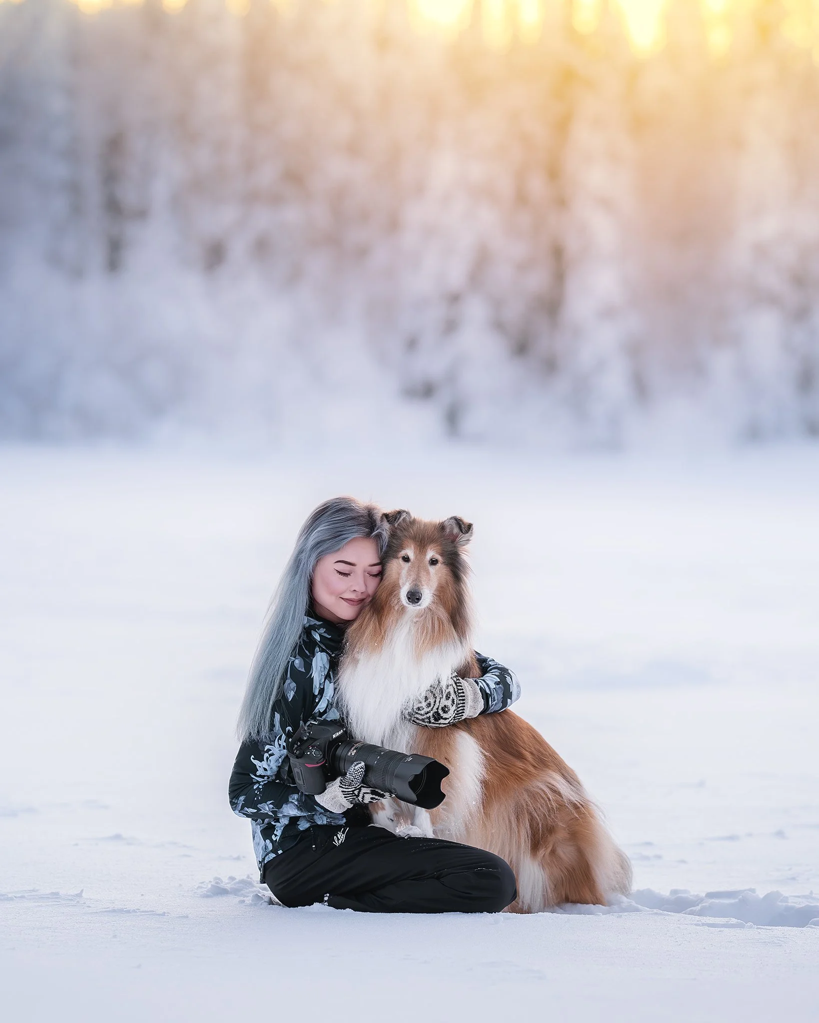 Nainen ja collie-henkilökoira talvimaisemassa, lumi ja jäädytetyt puut taustalla.