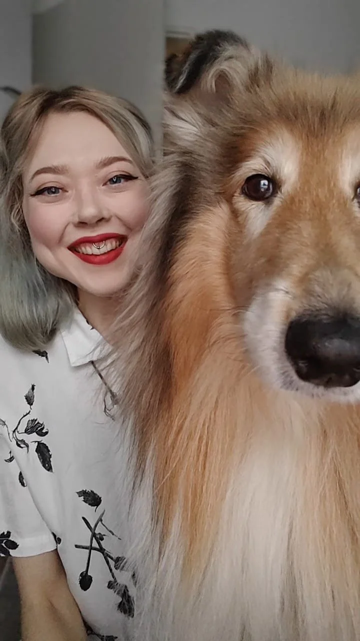 Nuori nainen hymyilee ja poseeraa suuren collie-koiran kanssa.
