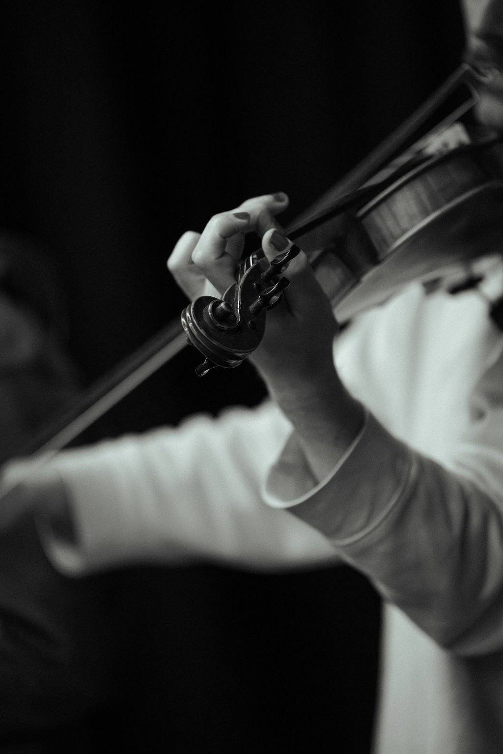 Close-up of hands playing violin with bow during MOV Dance Theatre rehearsal, scroll and pegs in sharp focus.