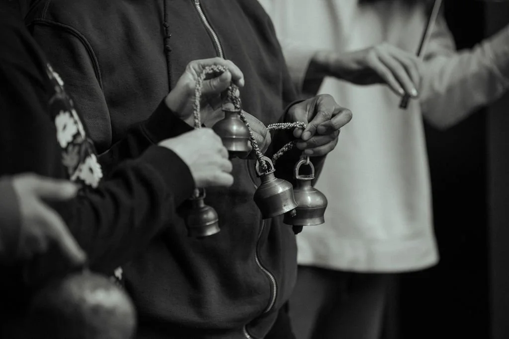 Close crop of MOV Dance Theatre performers' hands holding strings of small brass bells during rehearsal.