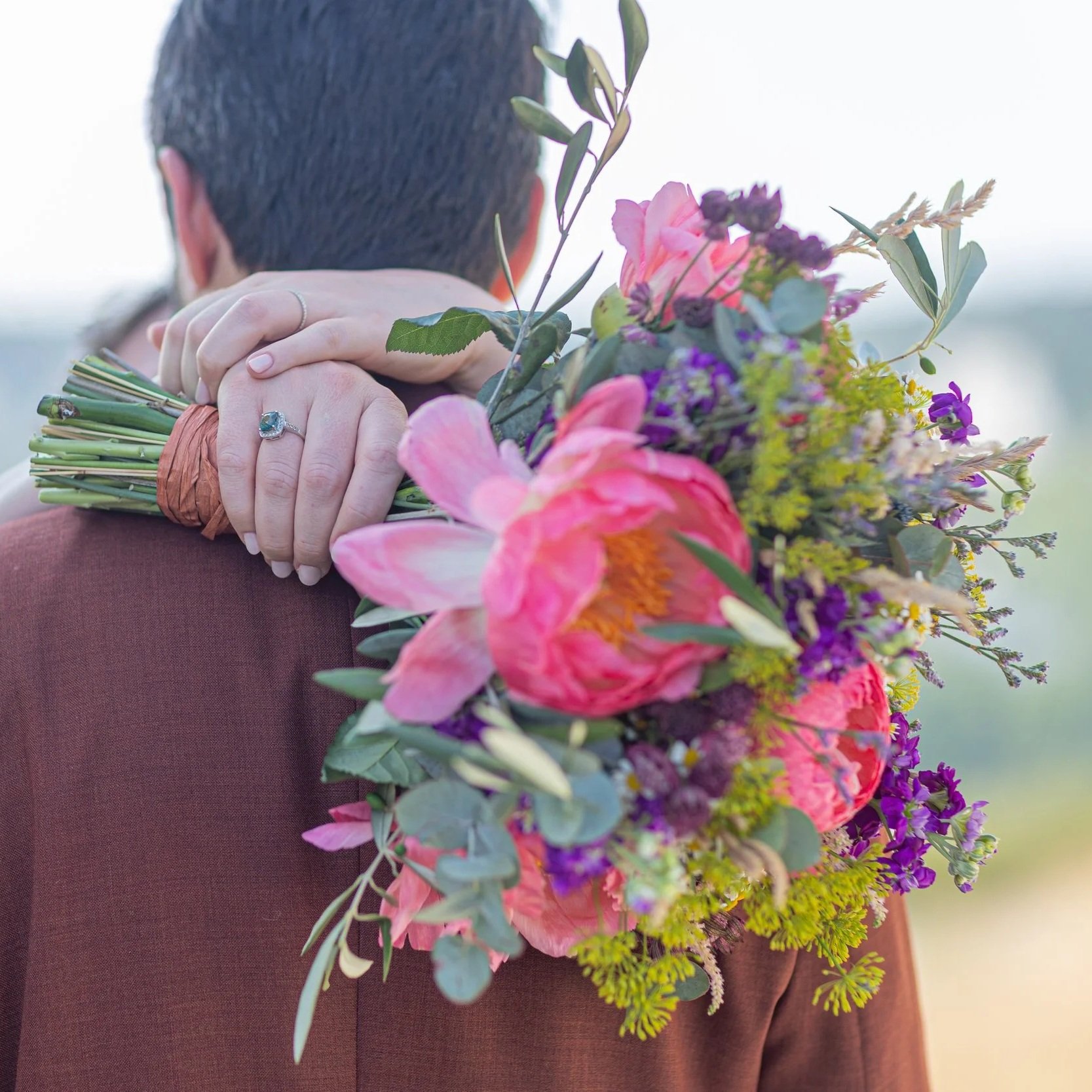 Un couple lors d'une cérémonie de mariage avec un bouquet de fleurs colorées sur l'épaule du marié.