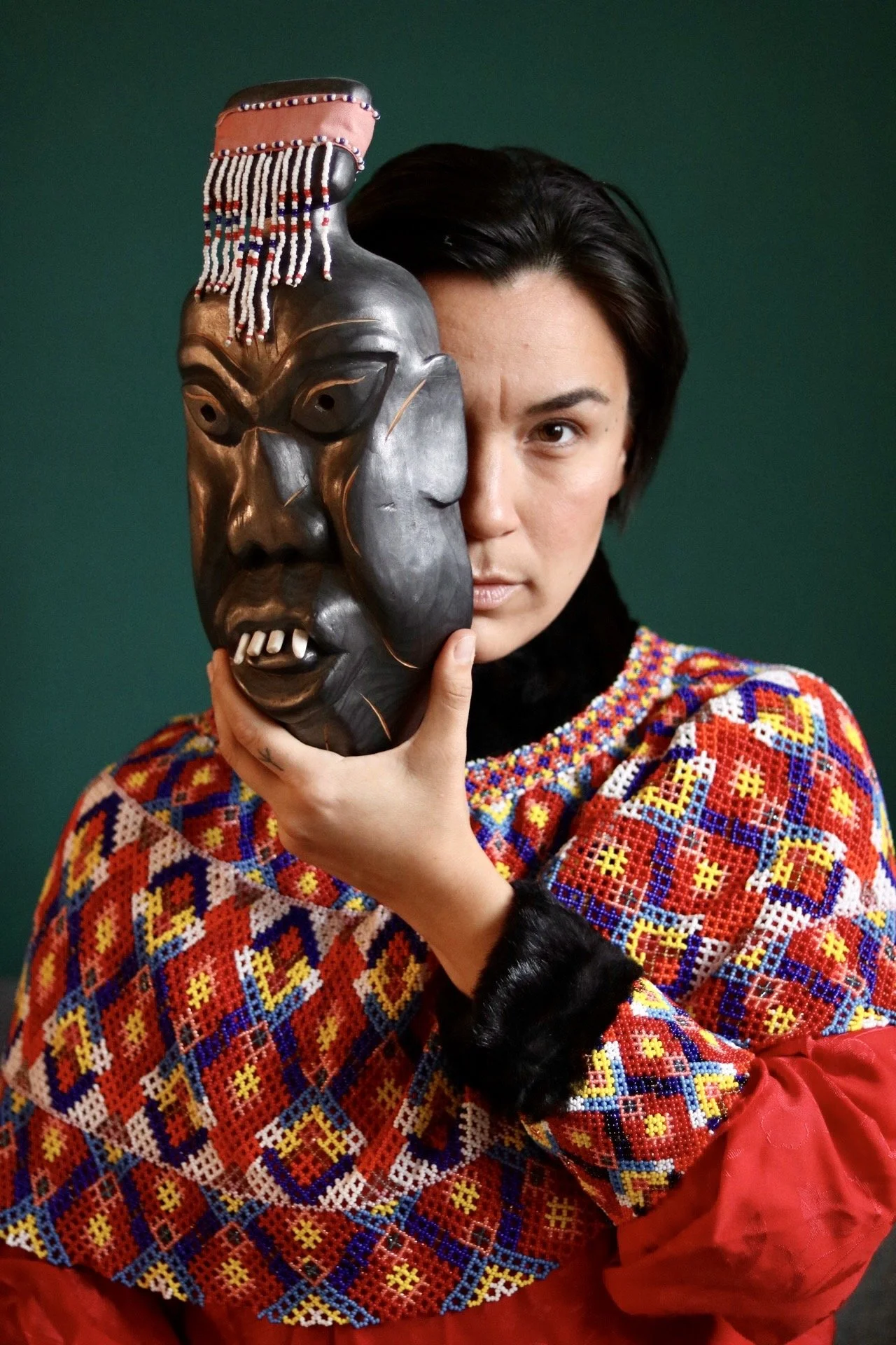 Grønlænder i nationaldragt, holder maske foran ansigtet. Greenlander holding mask in front of face, in national regalia