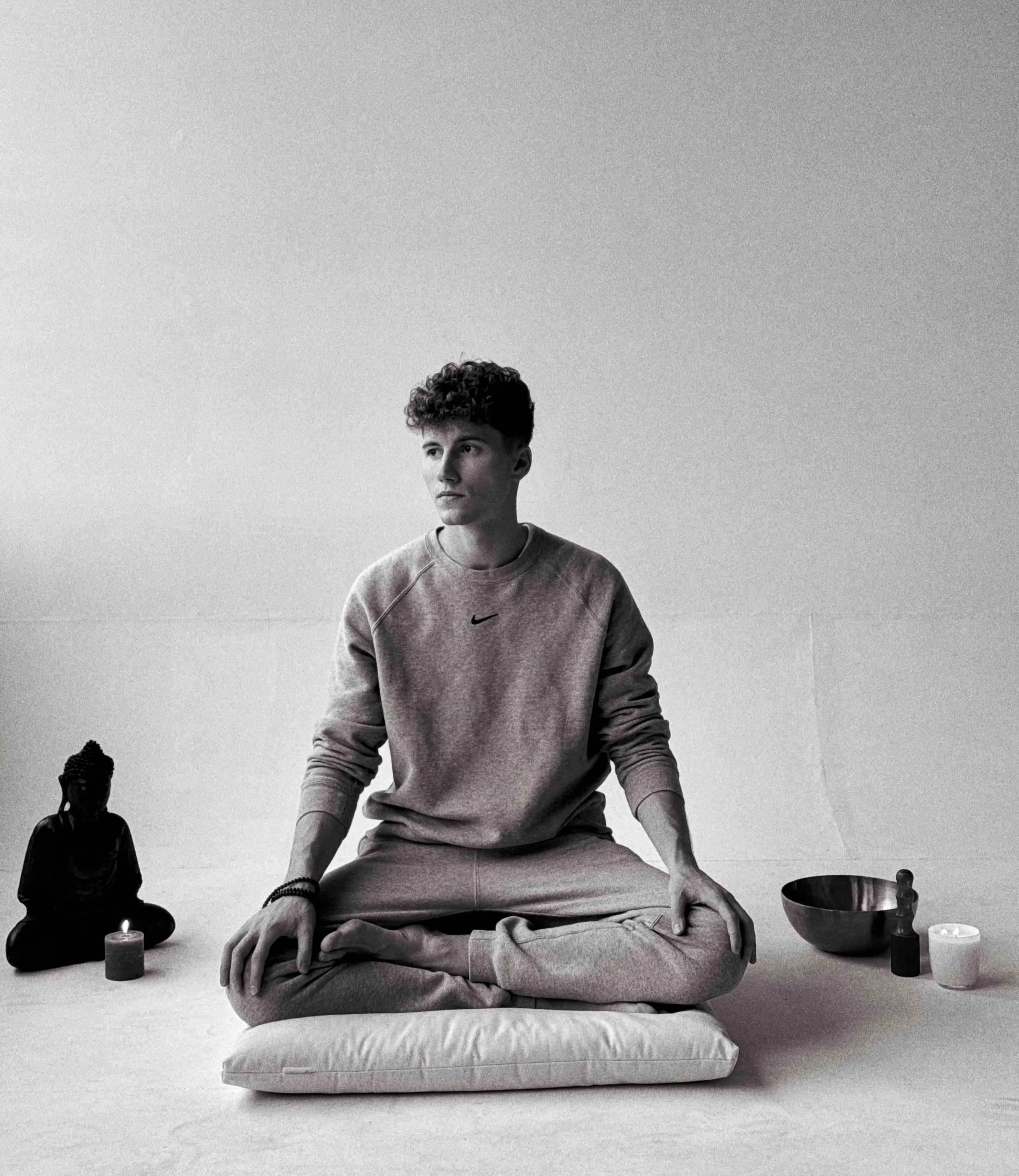 Meditace v klidném prostoru – sedící postava na polštáři se svíčkou, tibetskou mísou a sochou Buddhy