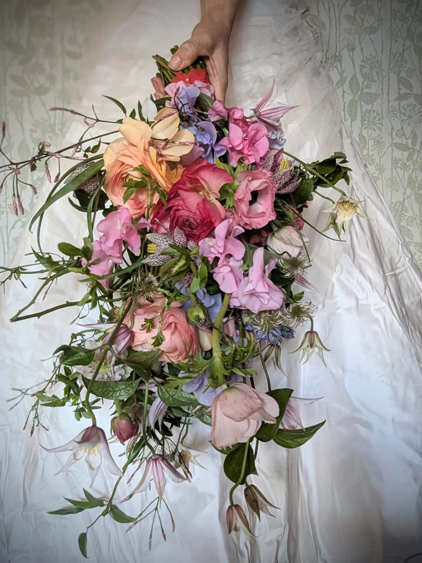 A bride holding a cascading wedding bouquet of colorful flowers over her wedding dress.