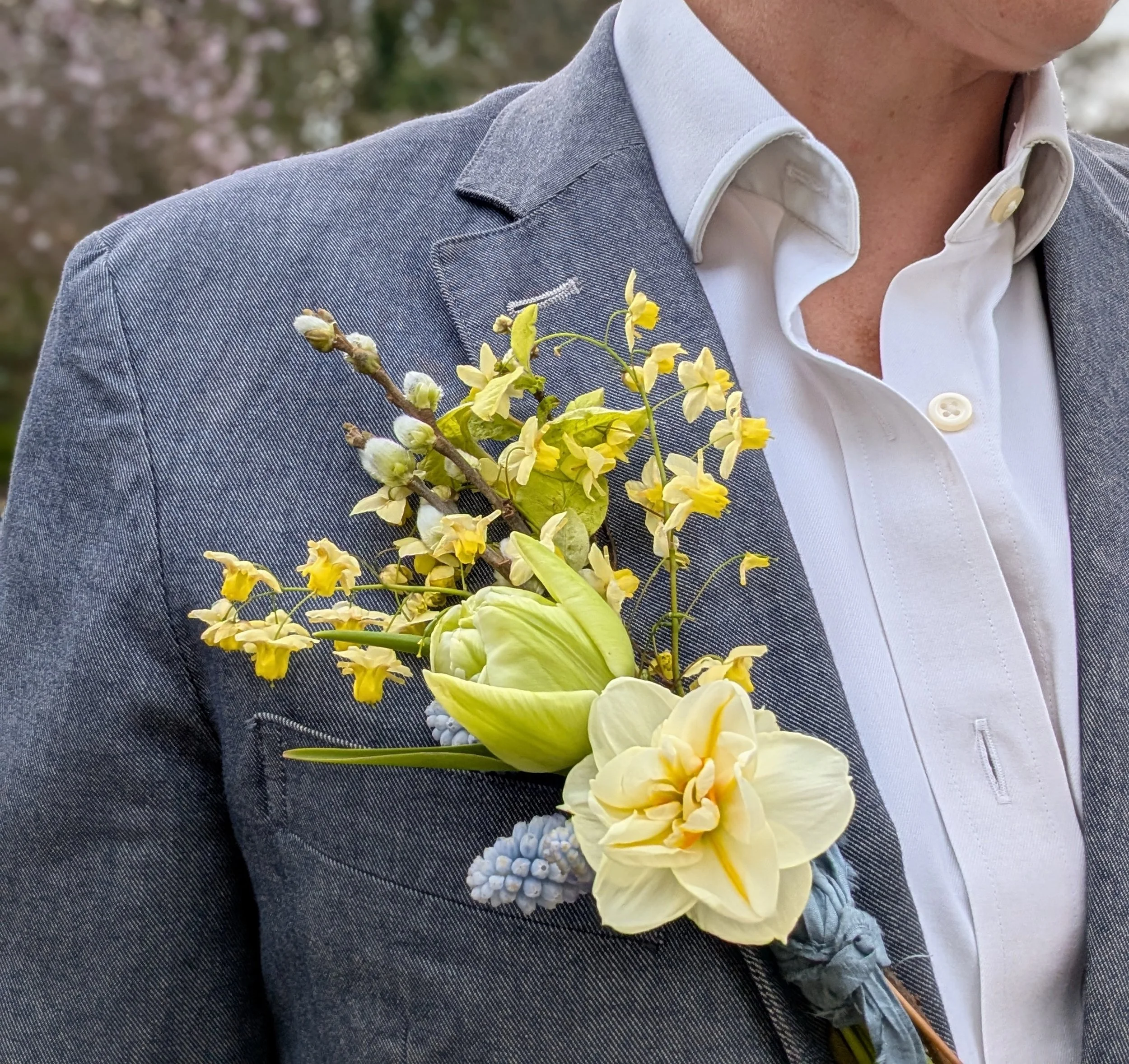 Close-up of a Groom in a linen suit wearing a white shirt, with a boutonniere made of yellow and white flowers pinned to the lapel.
