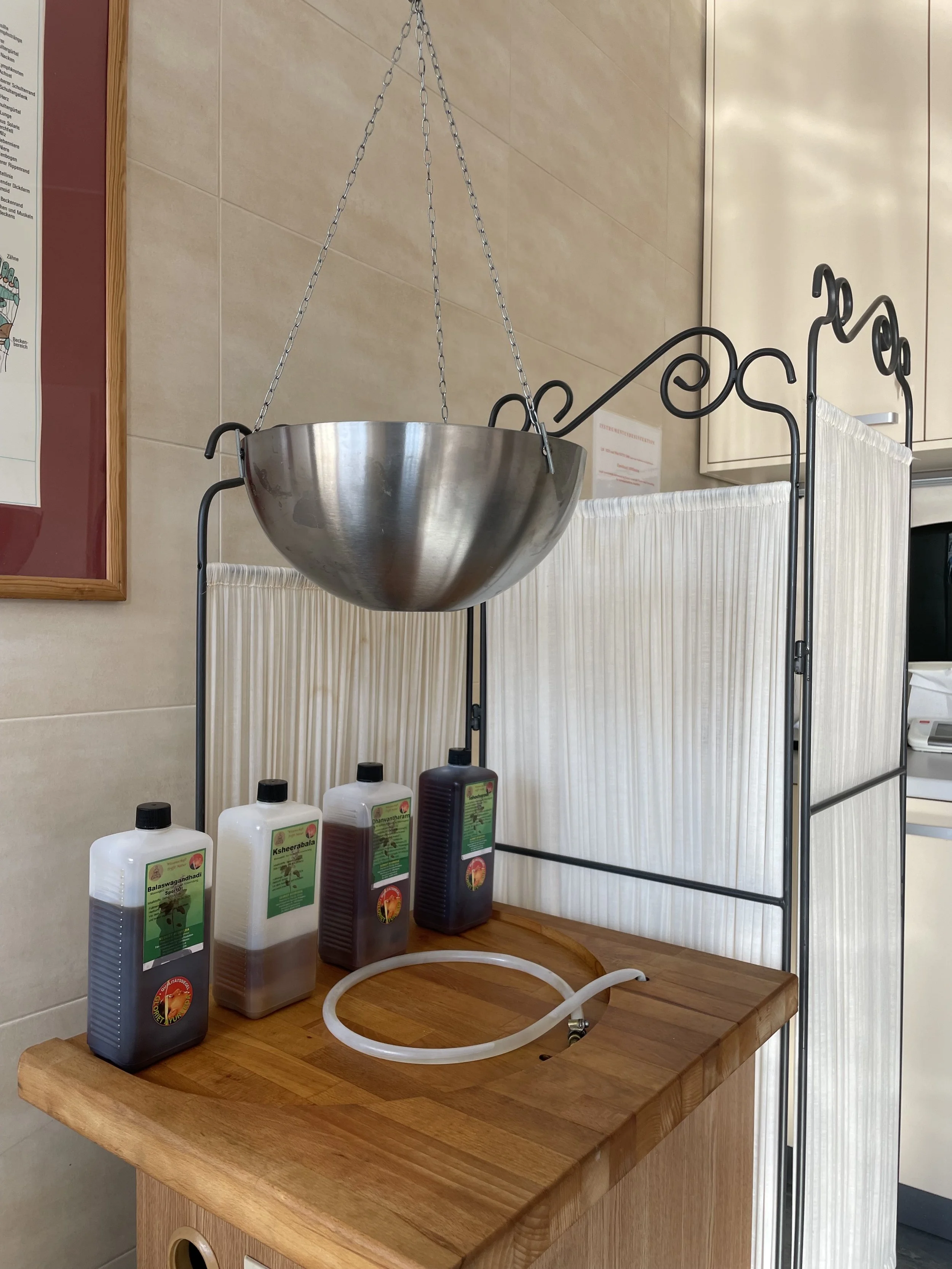 Ein Holztisch mit vier Flaschen mit verschiedenen Kräuter- oder Heilpflanzenlössungen, einer Schlauch, ein Metalltopf hängt an einem Gestell, im Hintergrund eine Küchenwand mit einer weißen Schürzwand.