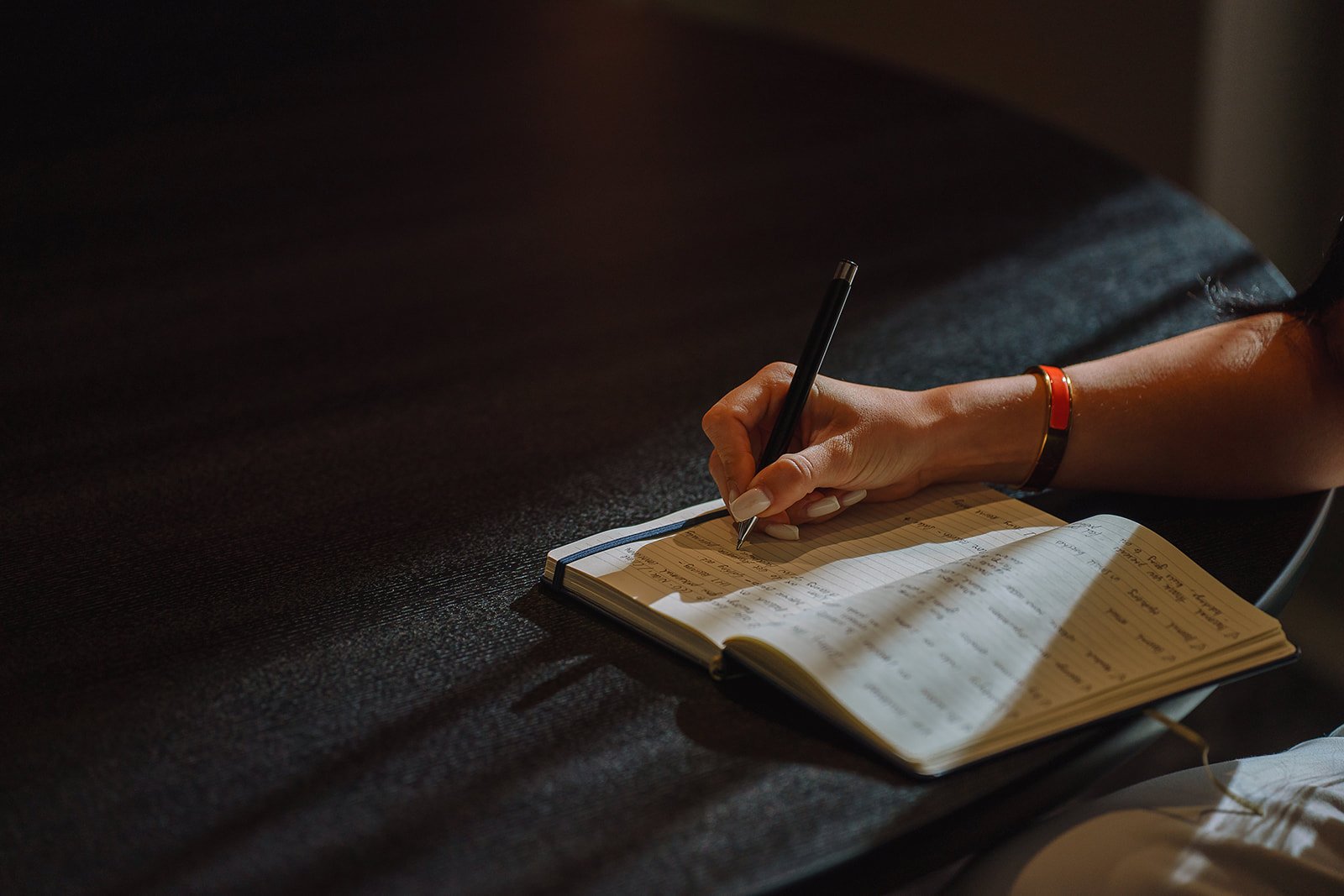 Person writing in an open notebook with a black pen at a desk