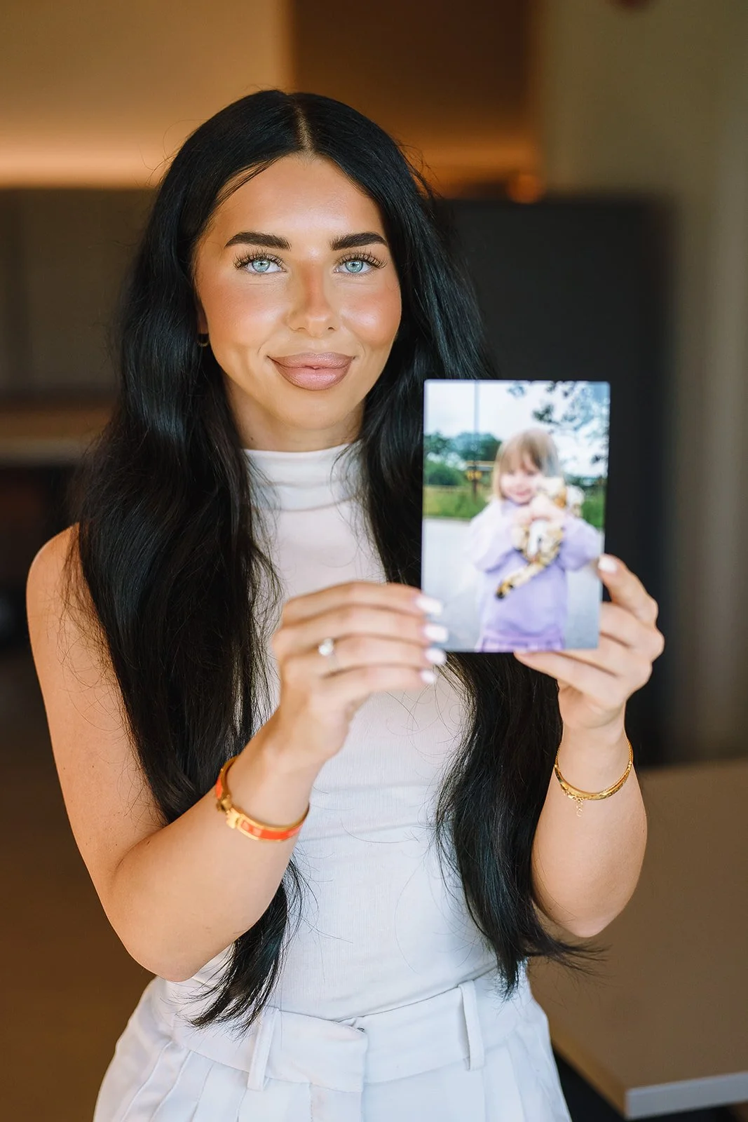 Woman with long dark hair holding a photo of a child outdoors